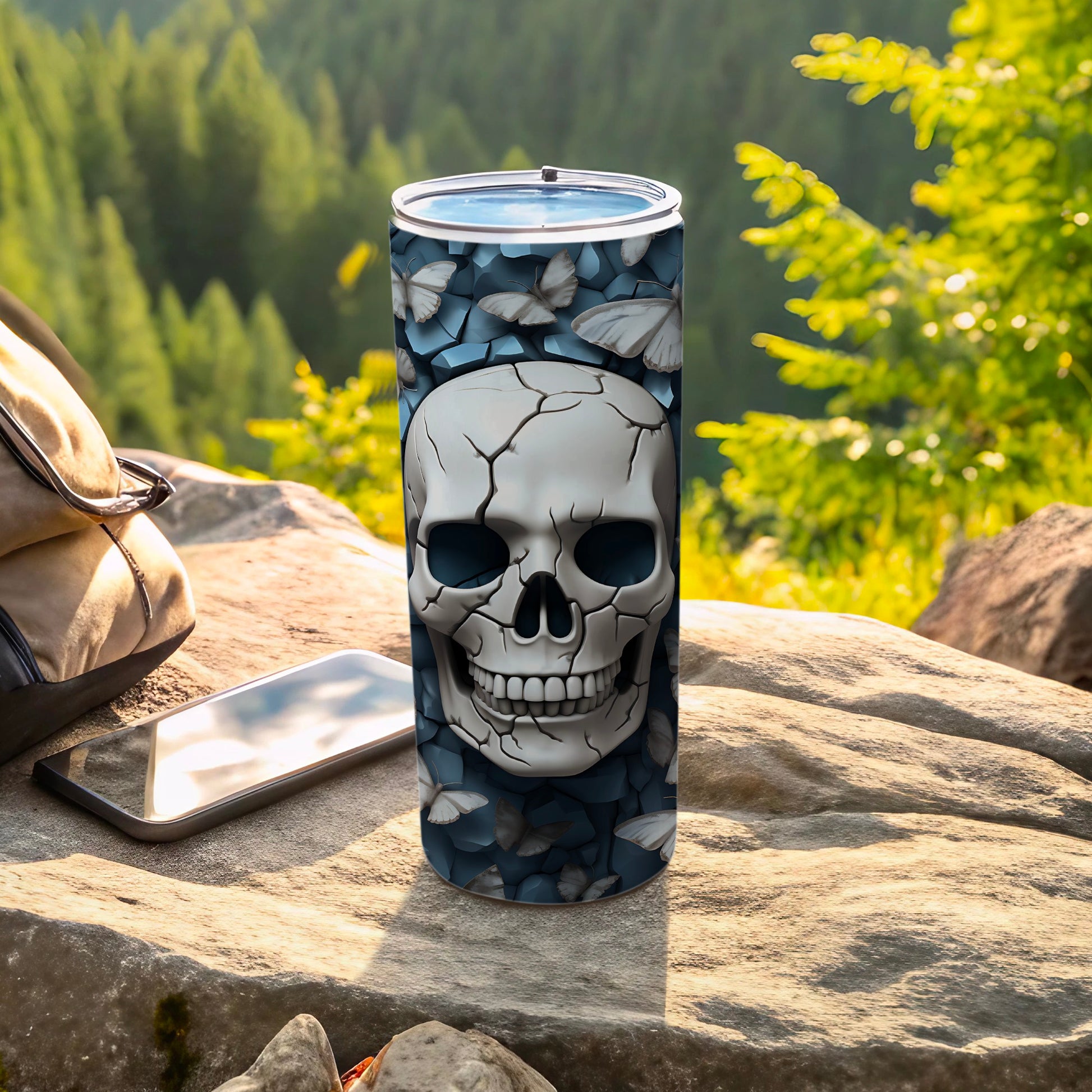 Glow-in-the-dark skull and moths tumbler on a rock with a backpack and phone.