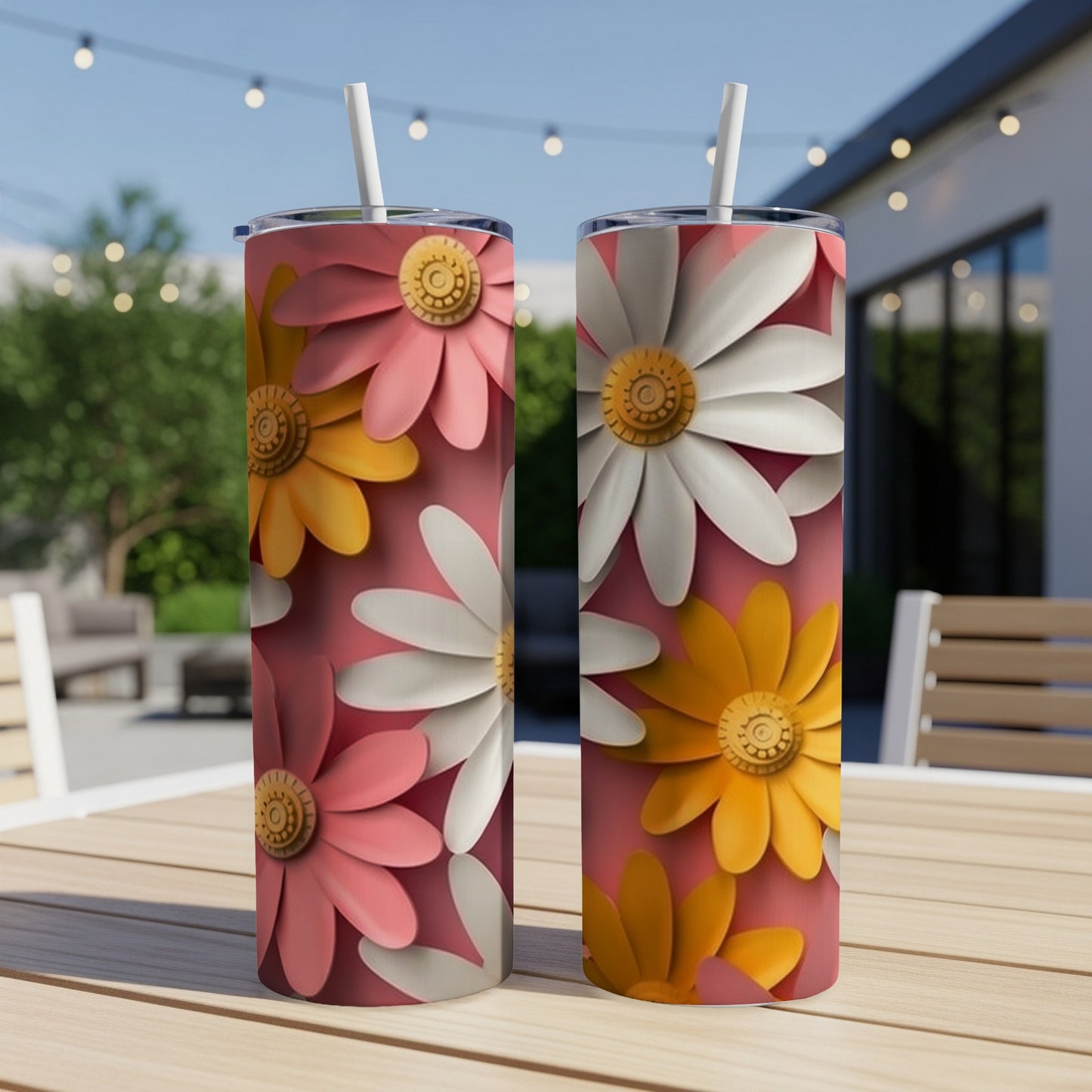 Two tumblers with pink, white, and yellow daisy designs on a patio table.
