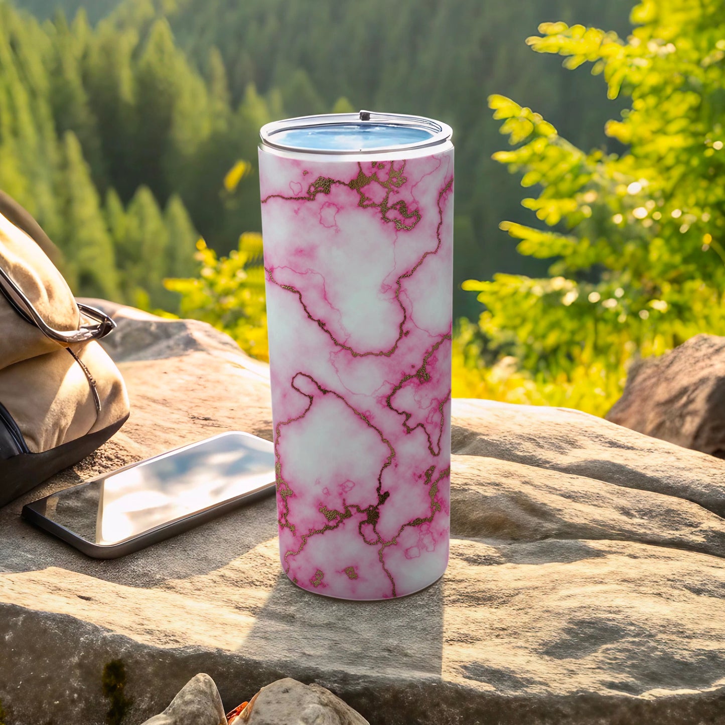 Pink marble tumbler with gold accents sits on rocks next to a phone.