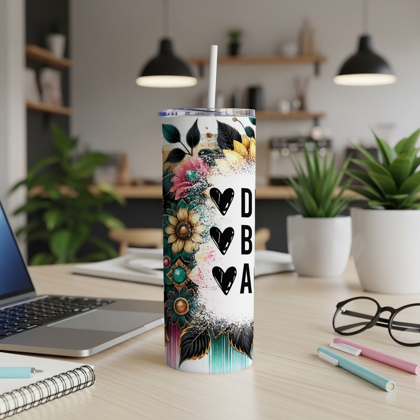 Tall tumbler with floral design and "DBA" text, on a desk.