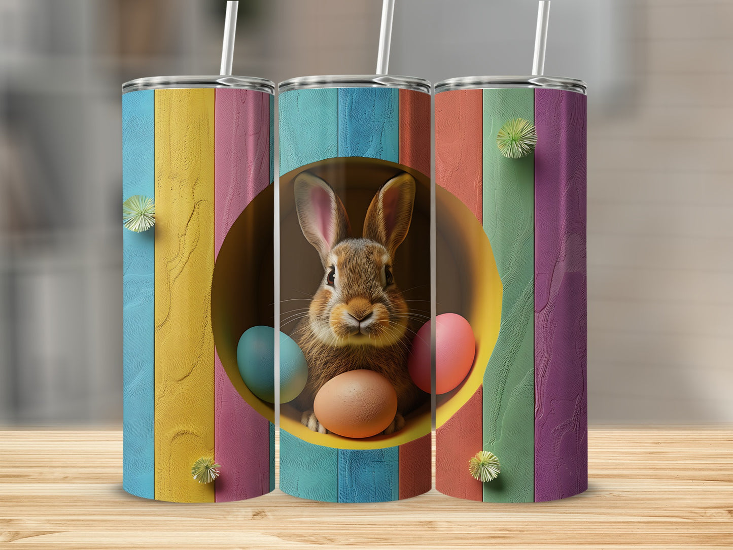 Three tumblers decorated with Easter eggs and a bunny against a colorful striped background.