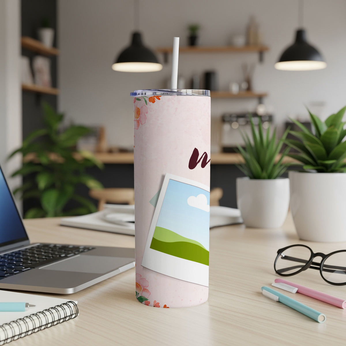Pink floral tumbler with a photo frame and straw on a desk.