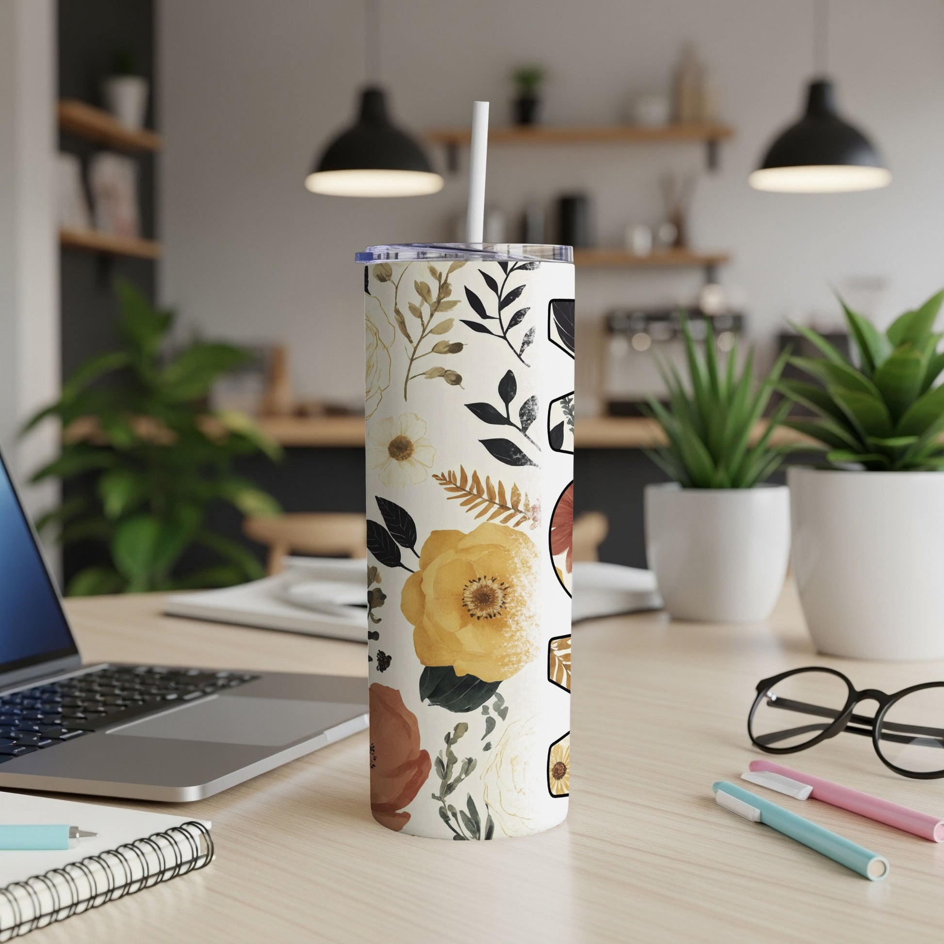 Floral patterned tumbler with straw on desk next to laptop and pens.