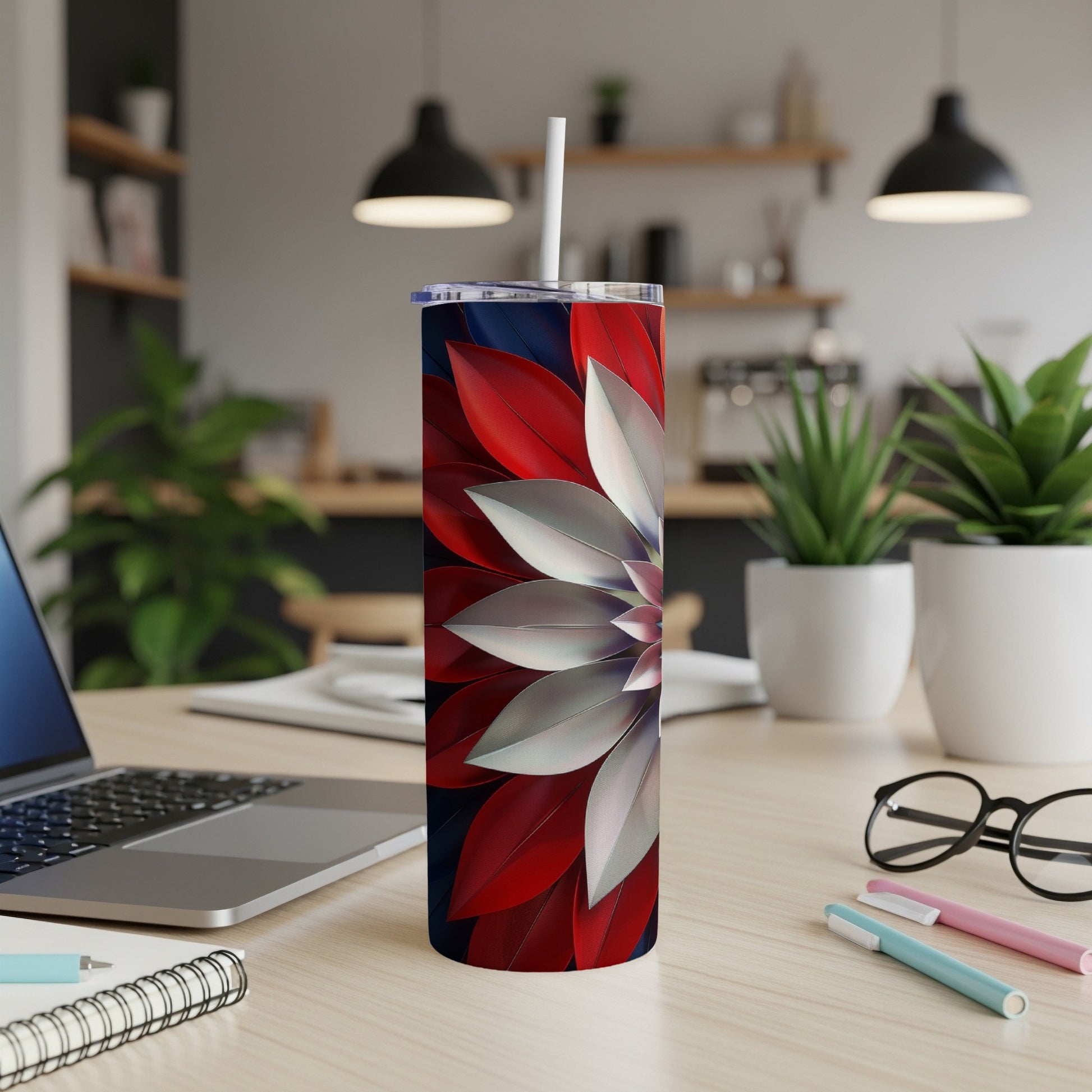 Red and silver floral pattern tumbler with straw on a desk.