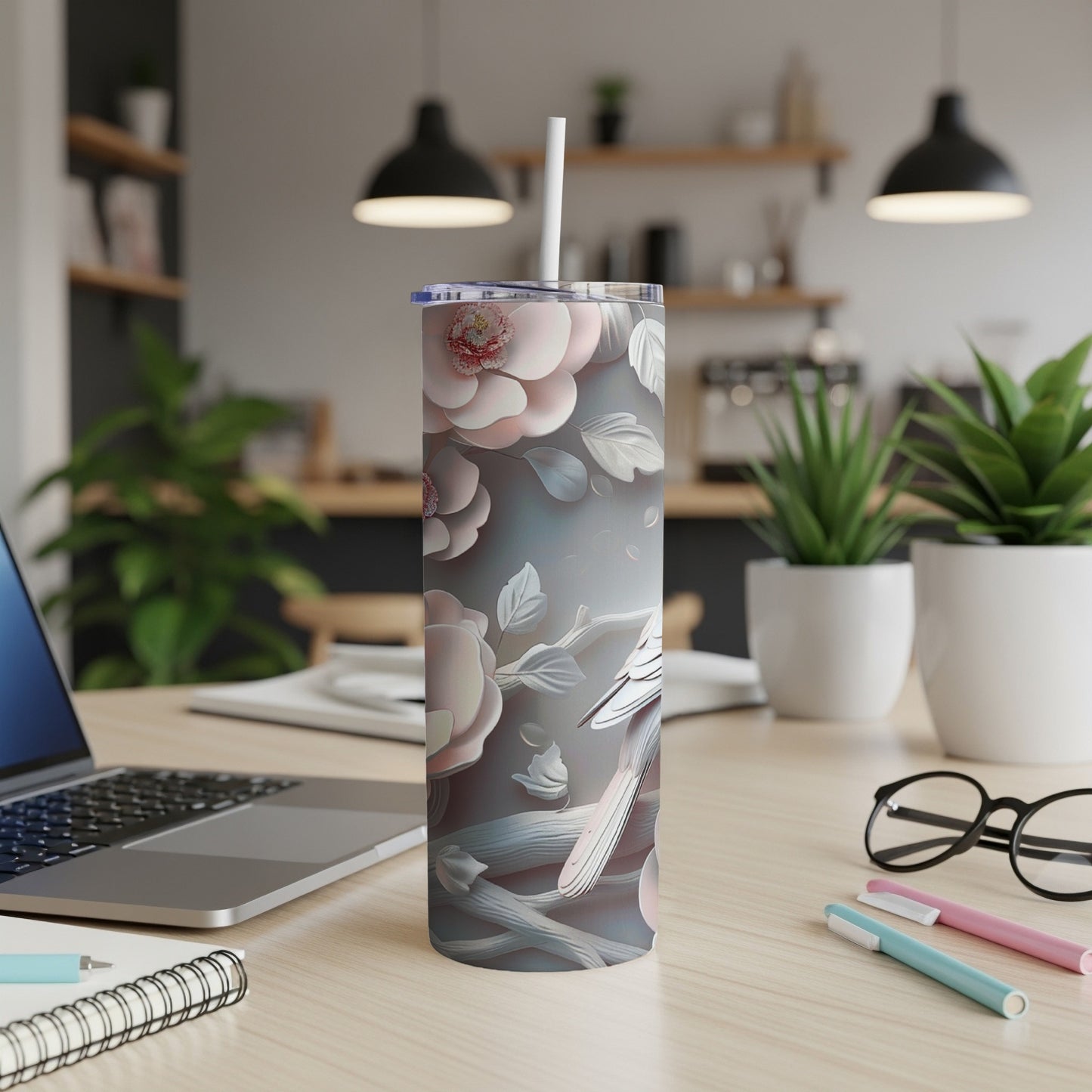 Floral patterned tumbler with straw on a desk with laptop and pens.
