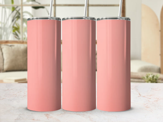 Three coral pink stainless steel tumblers with straws stand on a marble countertop.