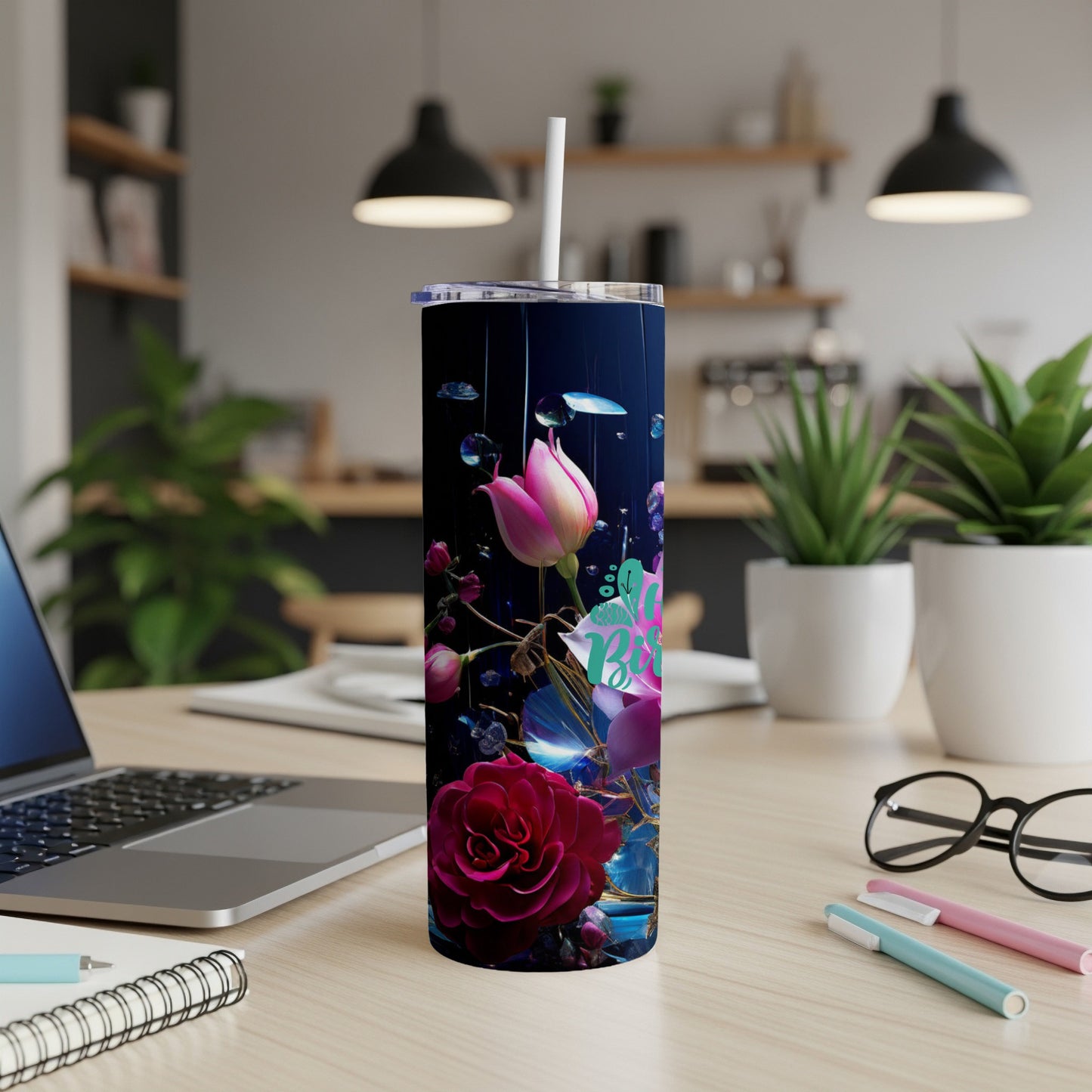 Dark tumbler with floral design and pink flowers, on a desk.