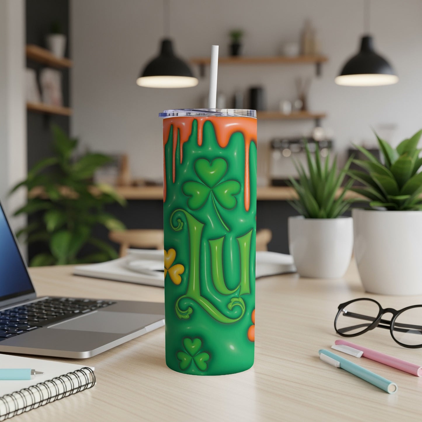 Green tumbler with orange drips and clover pattern, resting on a desk.