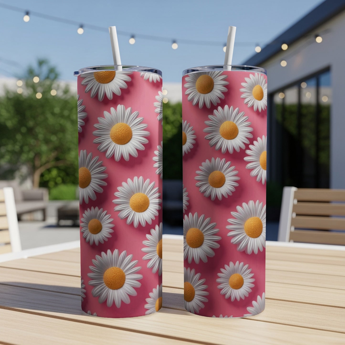 Two pink tumblers with white daisy pattern and straws on a table.