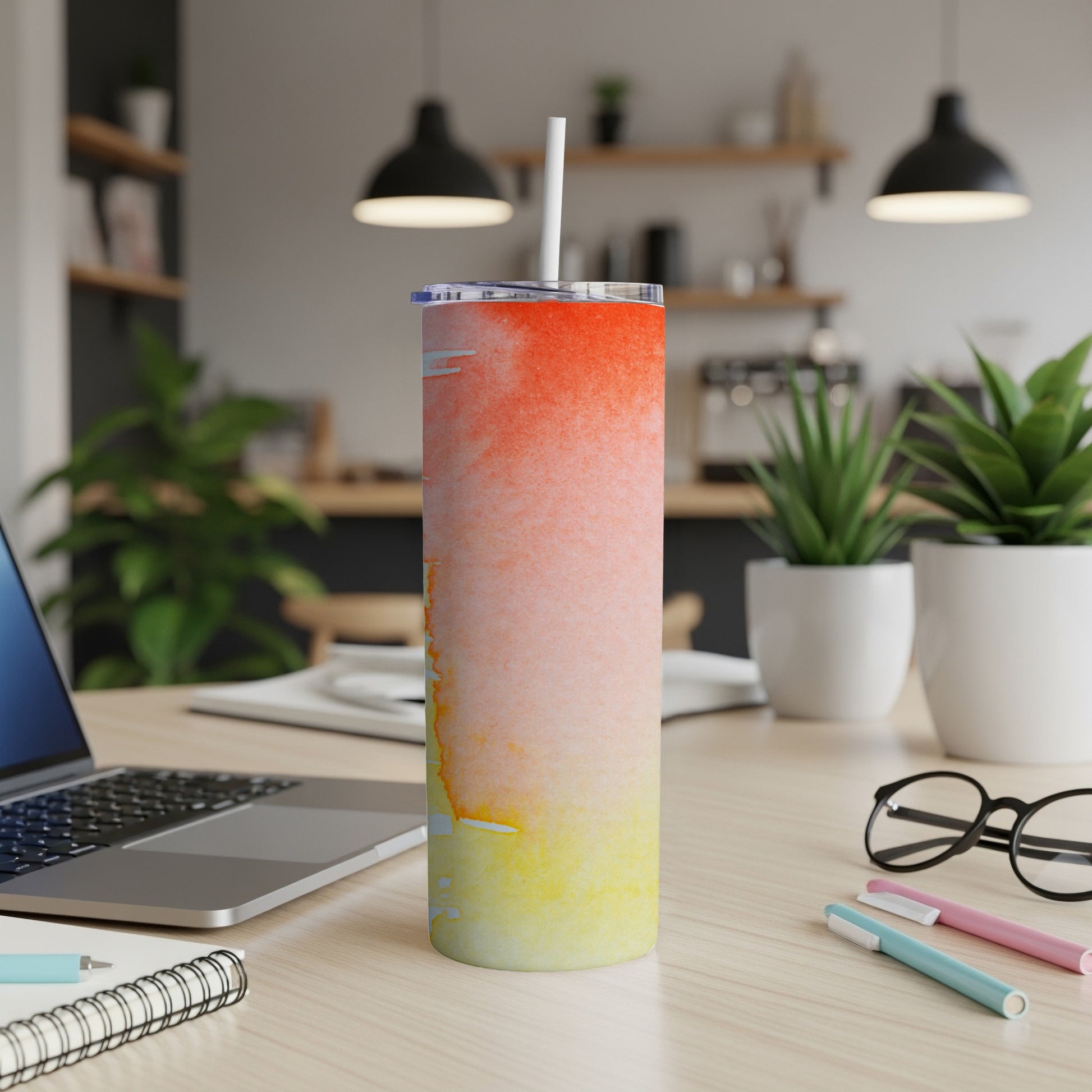 Tall tumbler with a watercolor sunset design sits on a desk.