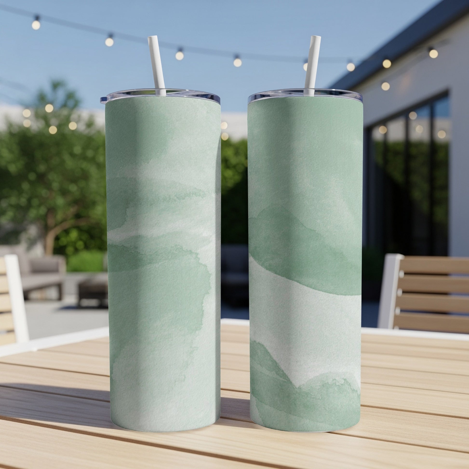 Two green watercolor print tumblers with straws on a wooden table.