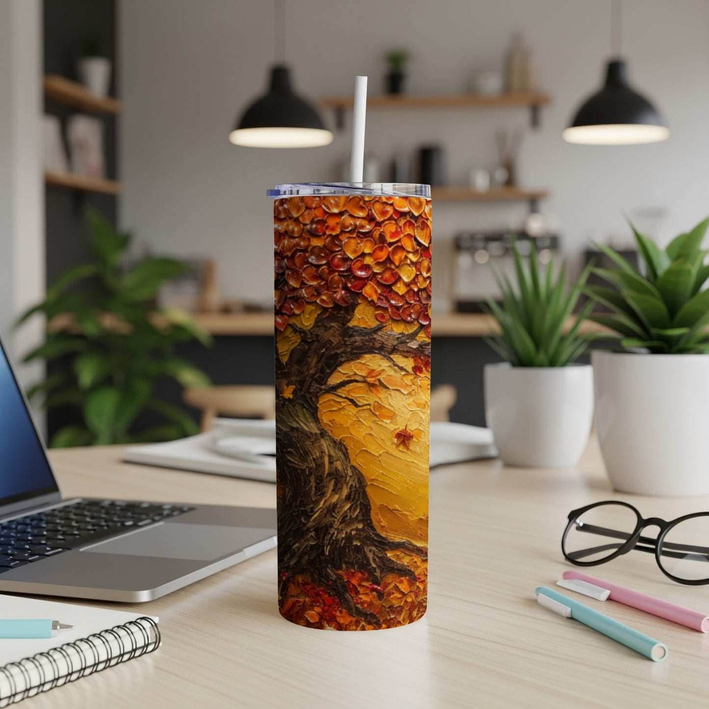 Tall tumbler with autumnal tree art, straw, and office desk.
