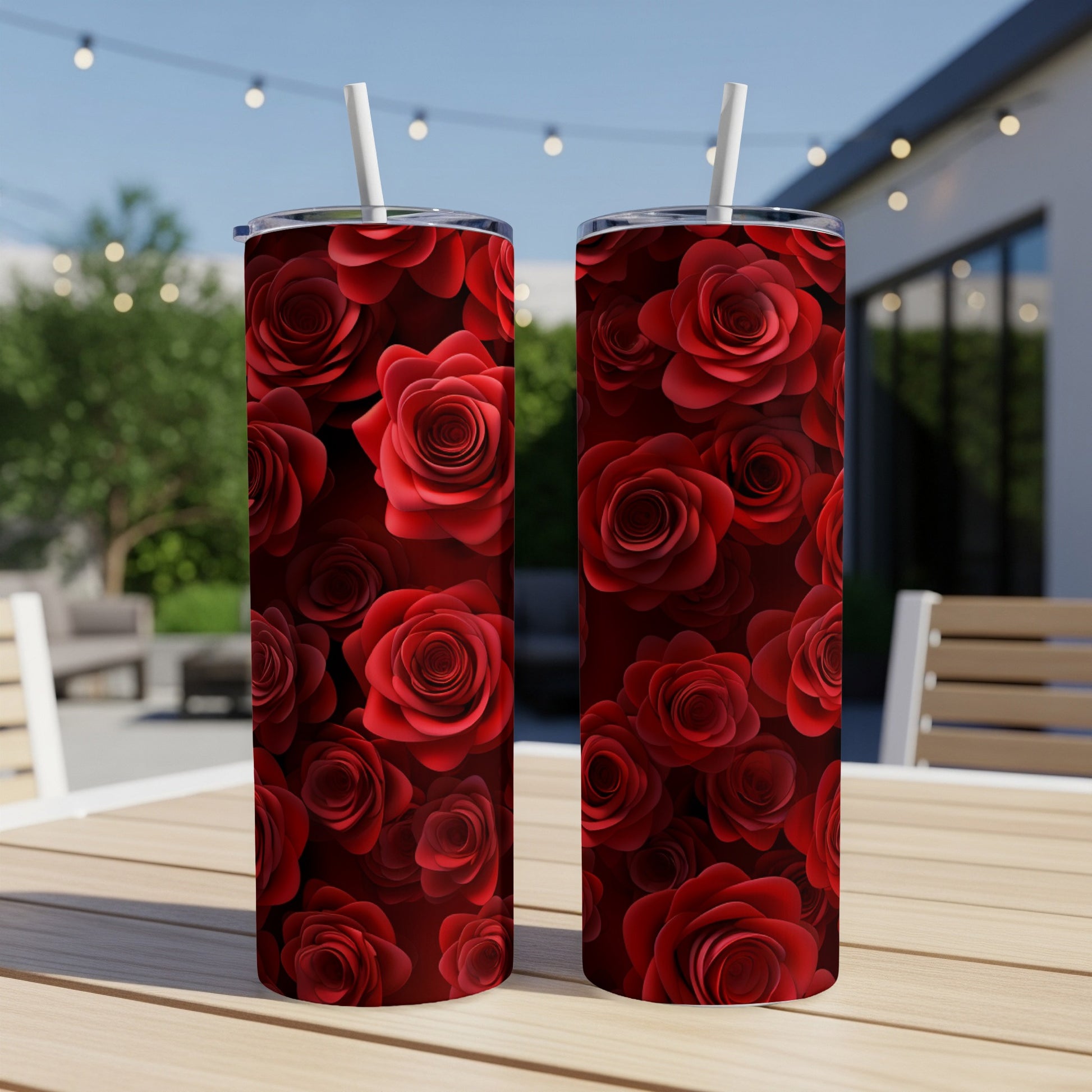 Two red rose patterned tumblers with straws on a wooden table.