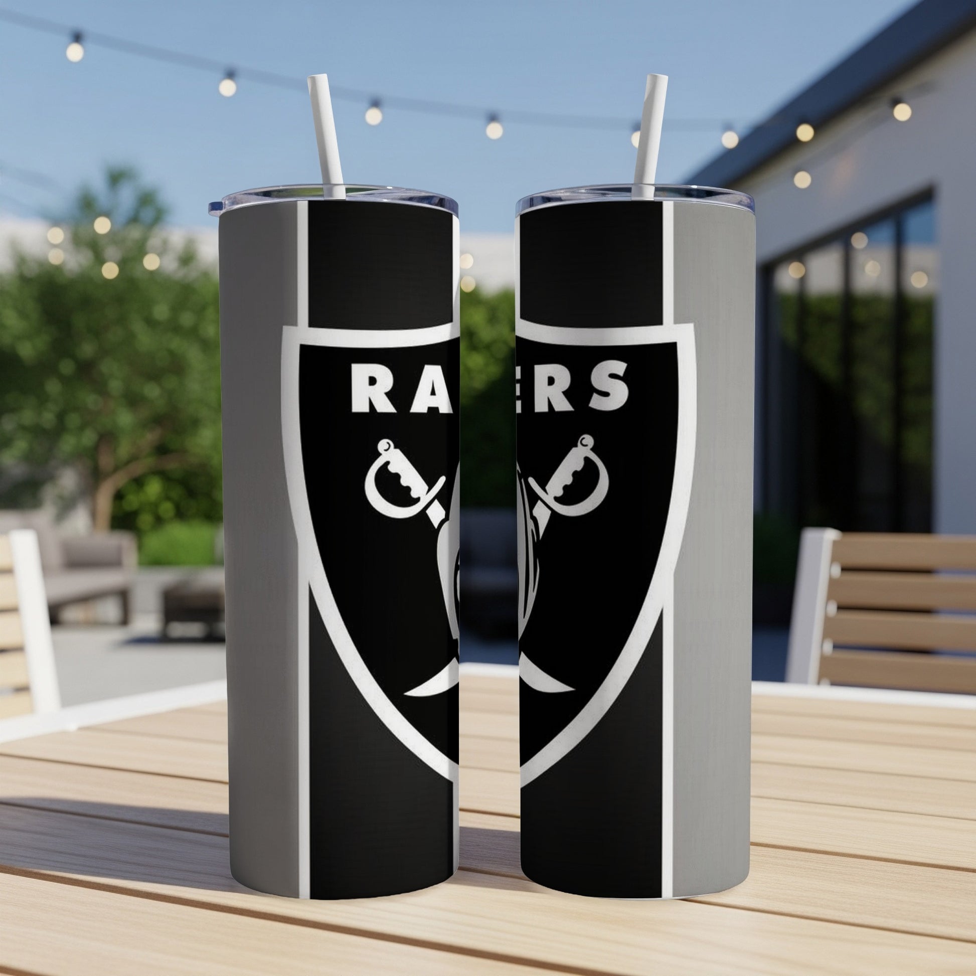 Two Las Vegas Raiders tumblers with white straws on a wooden table outdoors.
