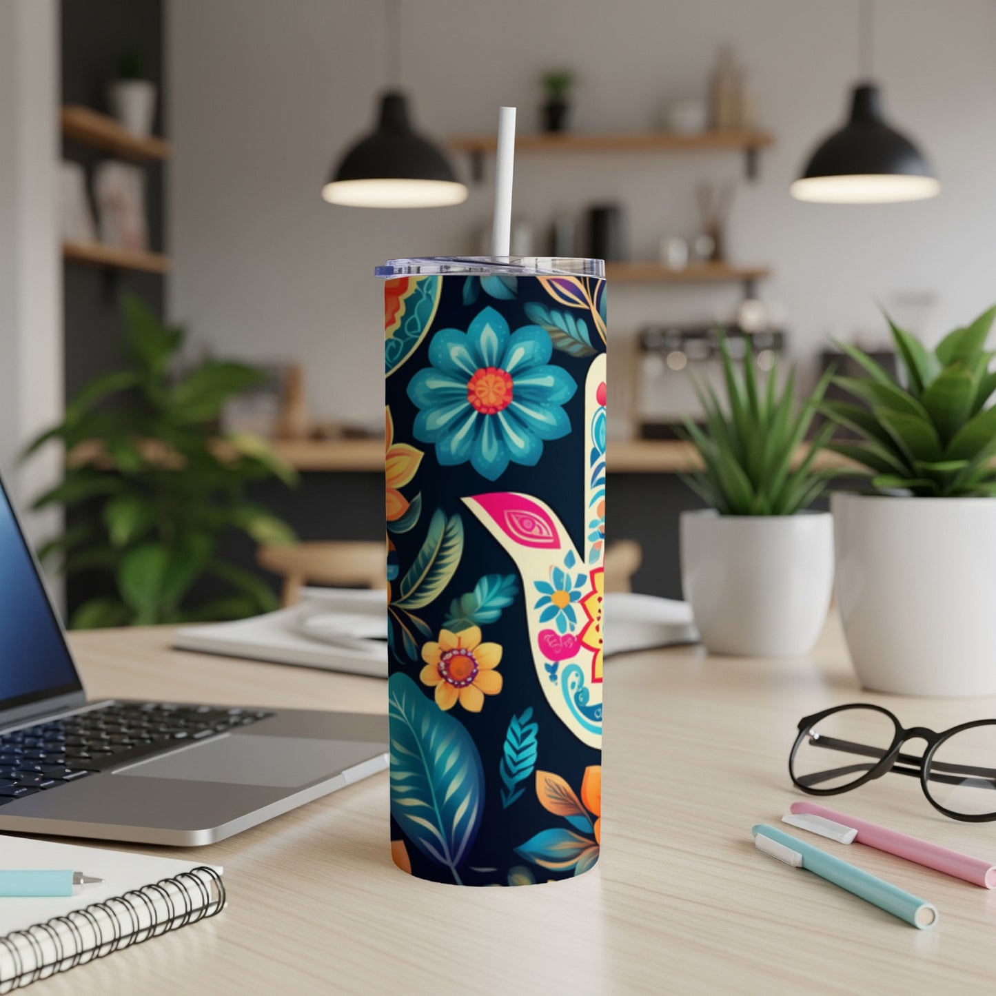 Floral patterned tumbler with straw on a desk with laptop and pens.
