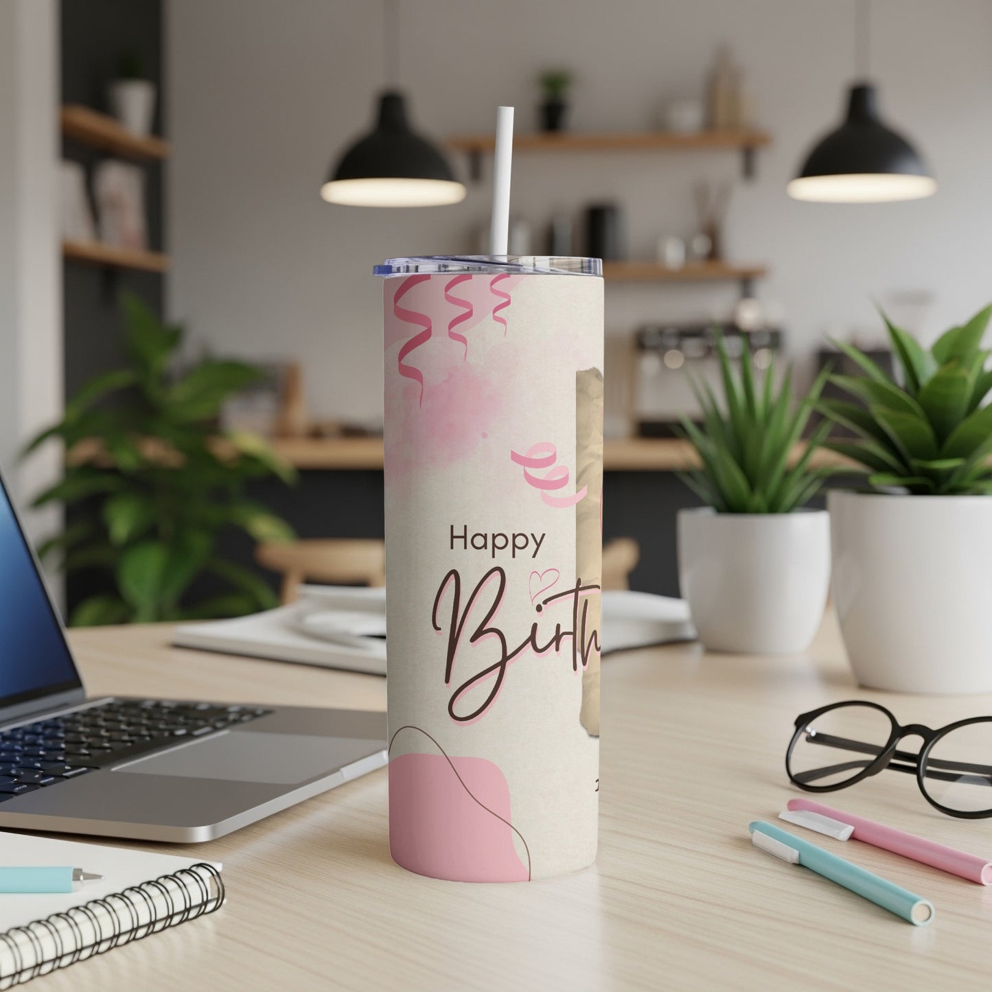 Tumbler with "Happy Birthday" text and pink ribbons on a desk.