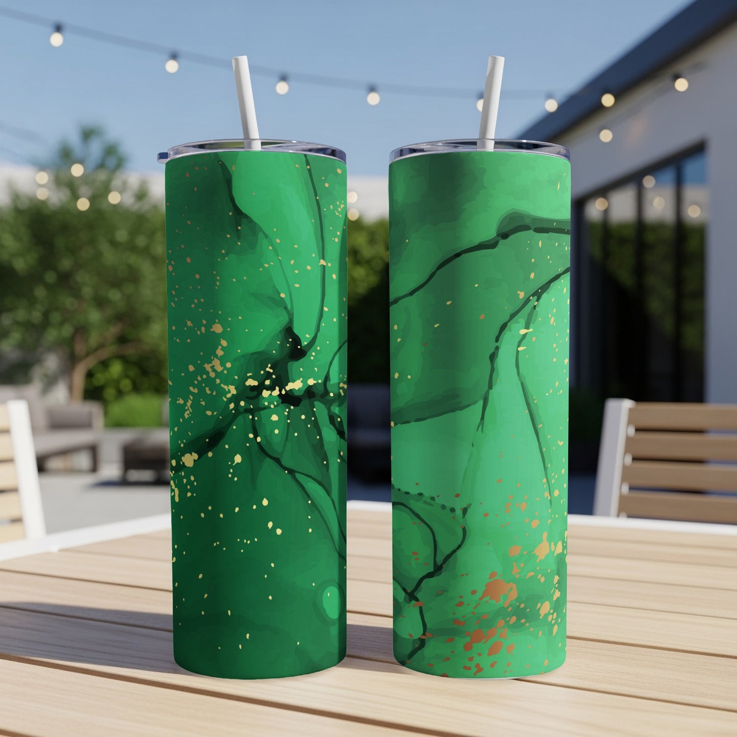 Two green tumblers with abstract gold marbling patterns sit on a table outdoors.
