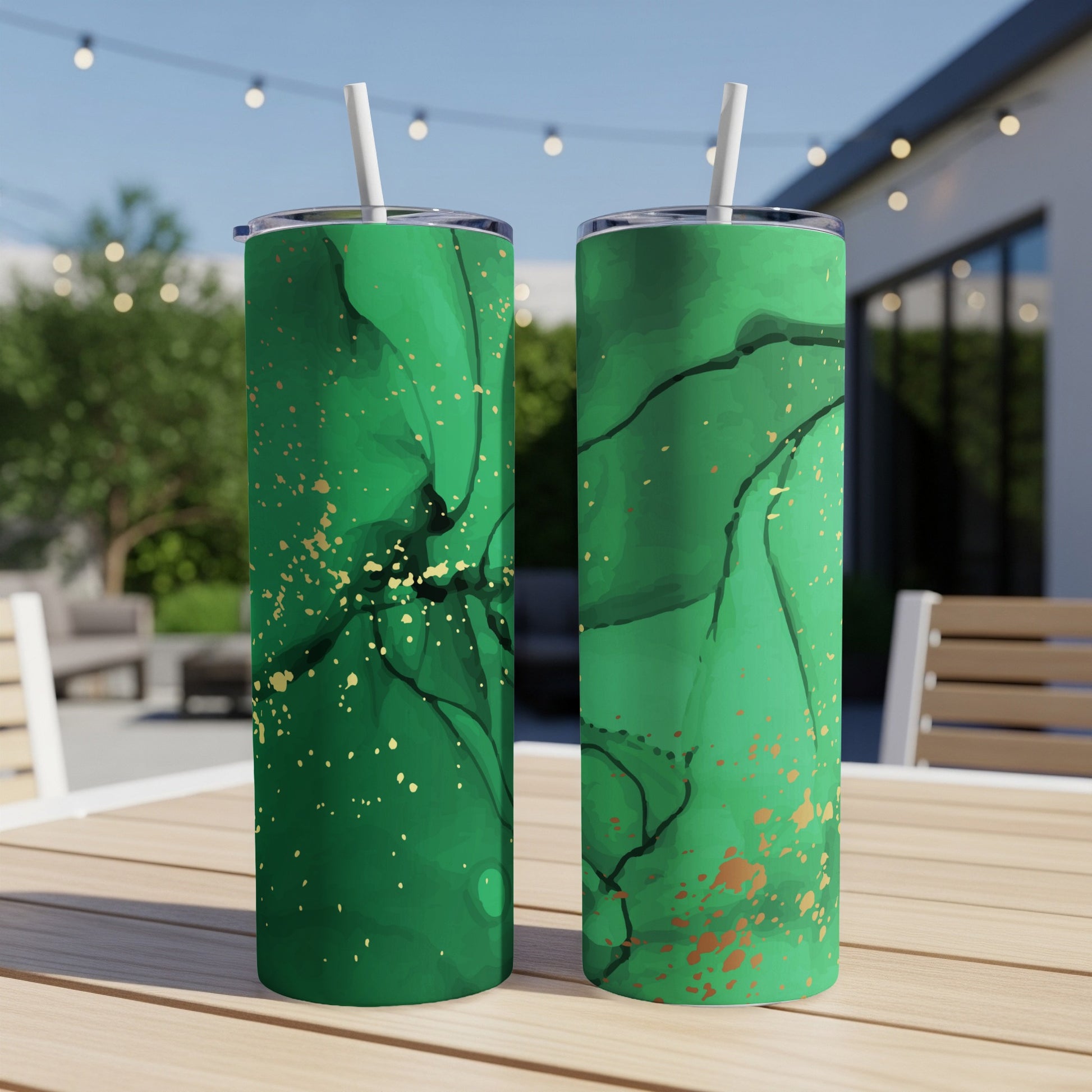 Two green tumblers with abstract gold marbling patterns sit on a table outdoors.