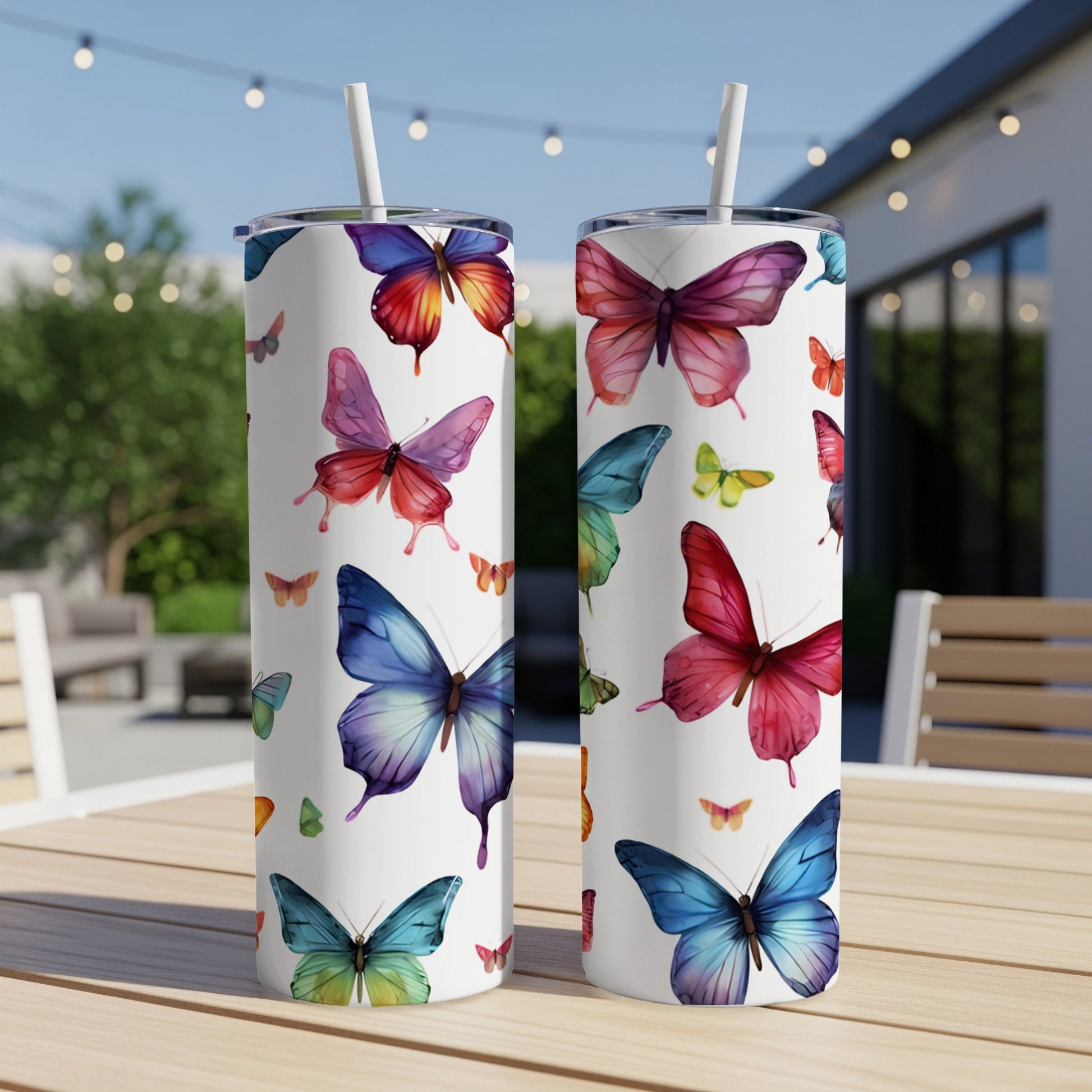 Two white tumblers with colorful butterfly designs on a wooden table.