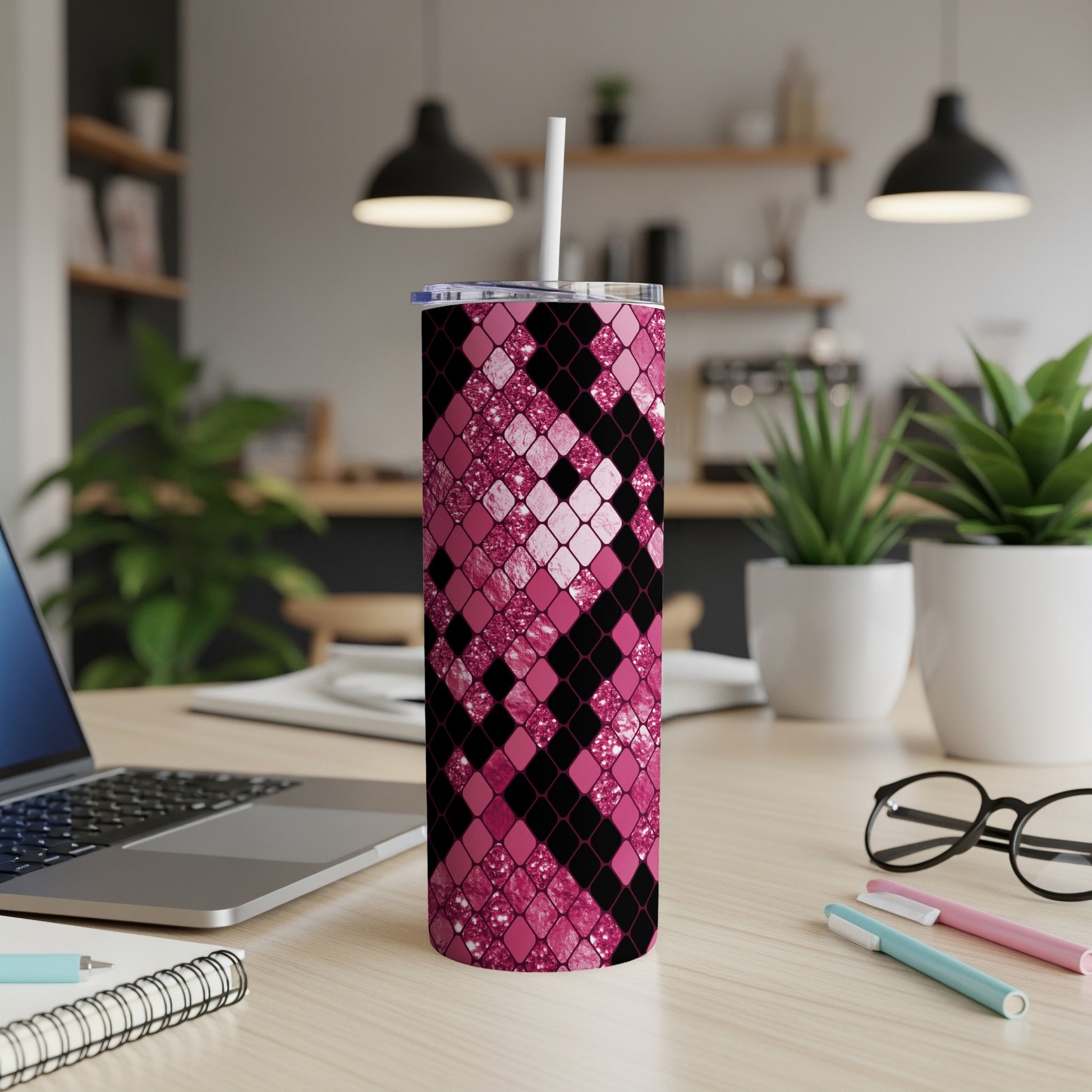 Pink diamond pattern tumbler with straw on desk beside laptop and glasses.