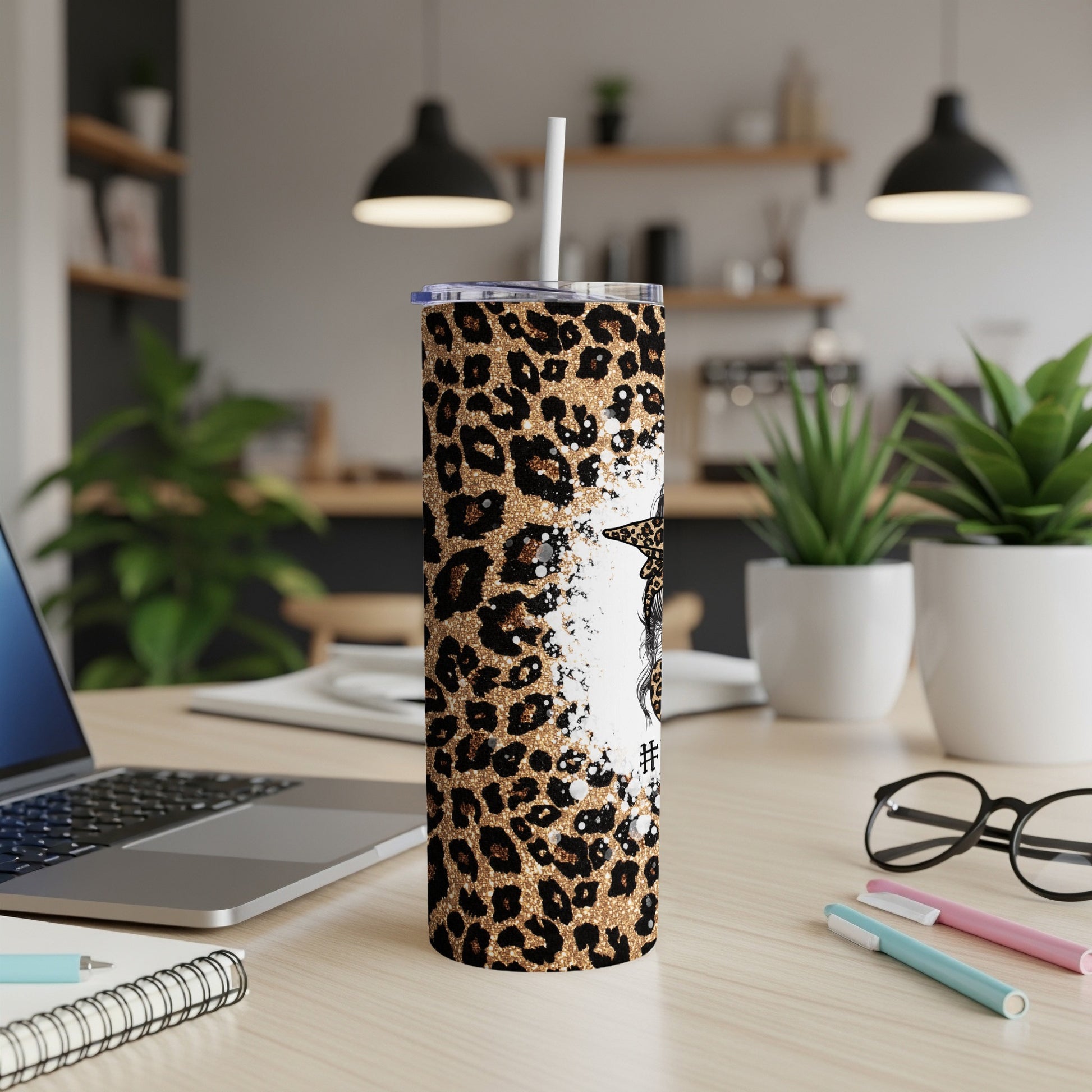Leopard print tumbler with straw, laptop, and pens on desk.