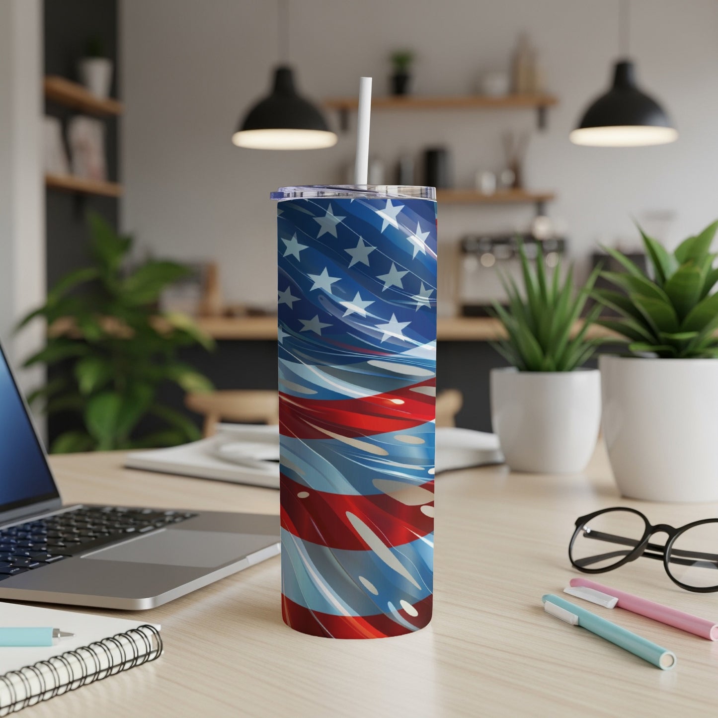 Tall tumbler with American flag design and straw on a wooden desk.