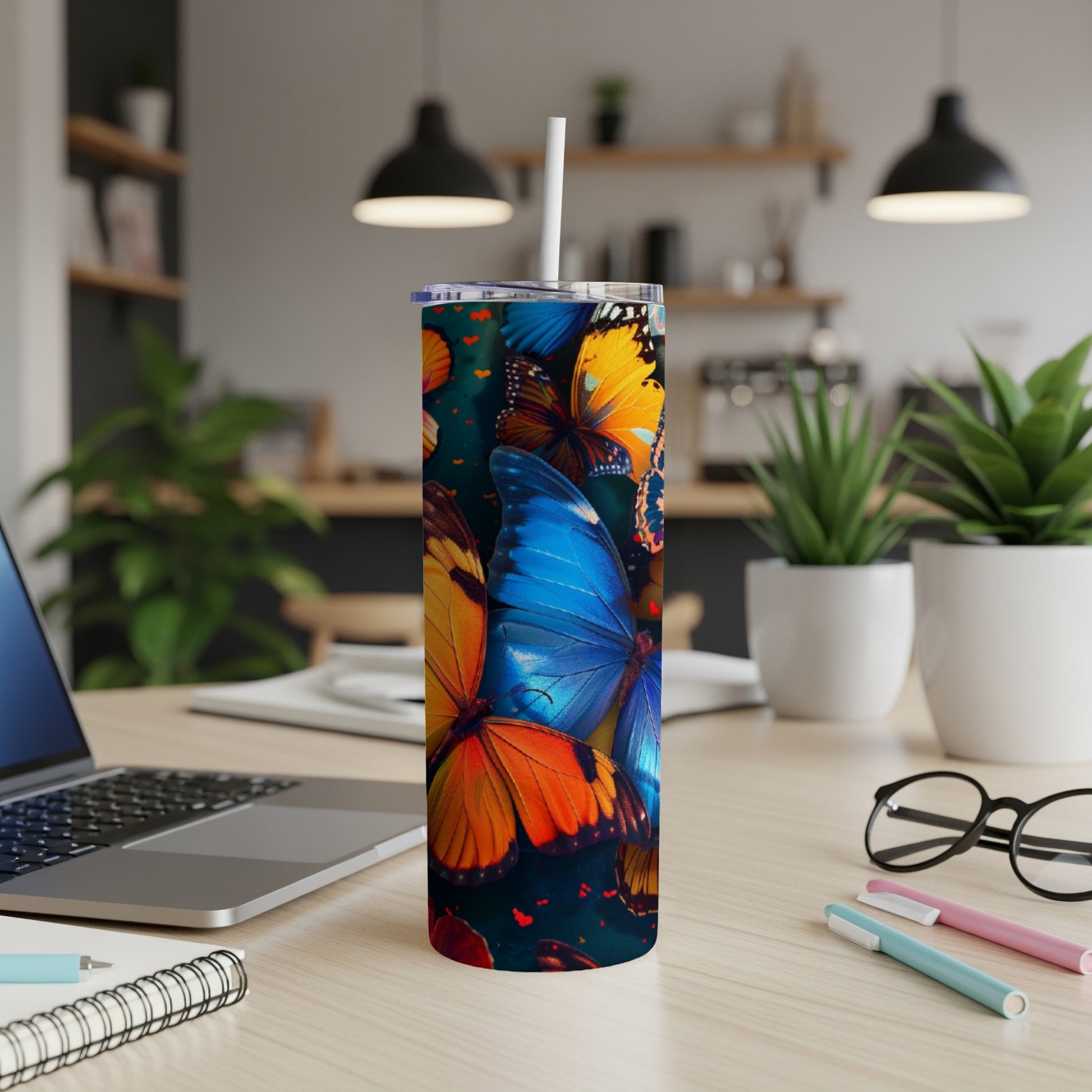 Tall tumbler with colorful butterflies and a straw, on a desk.