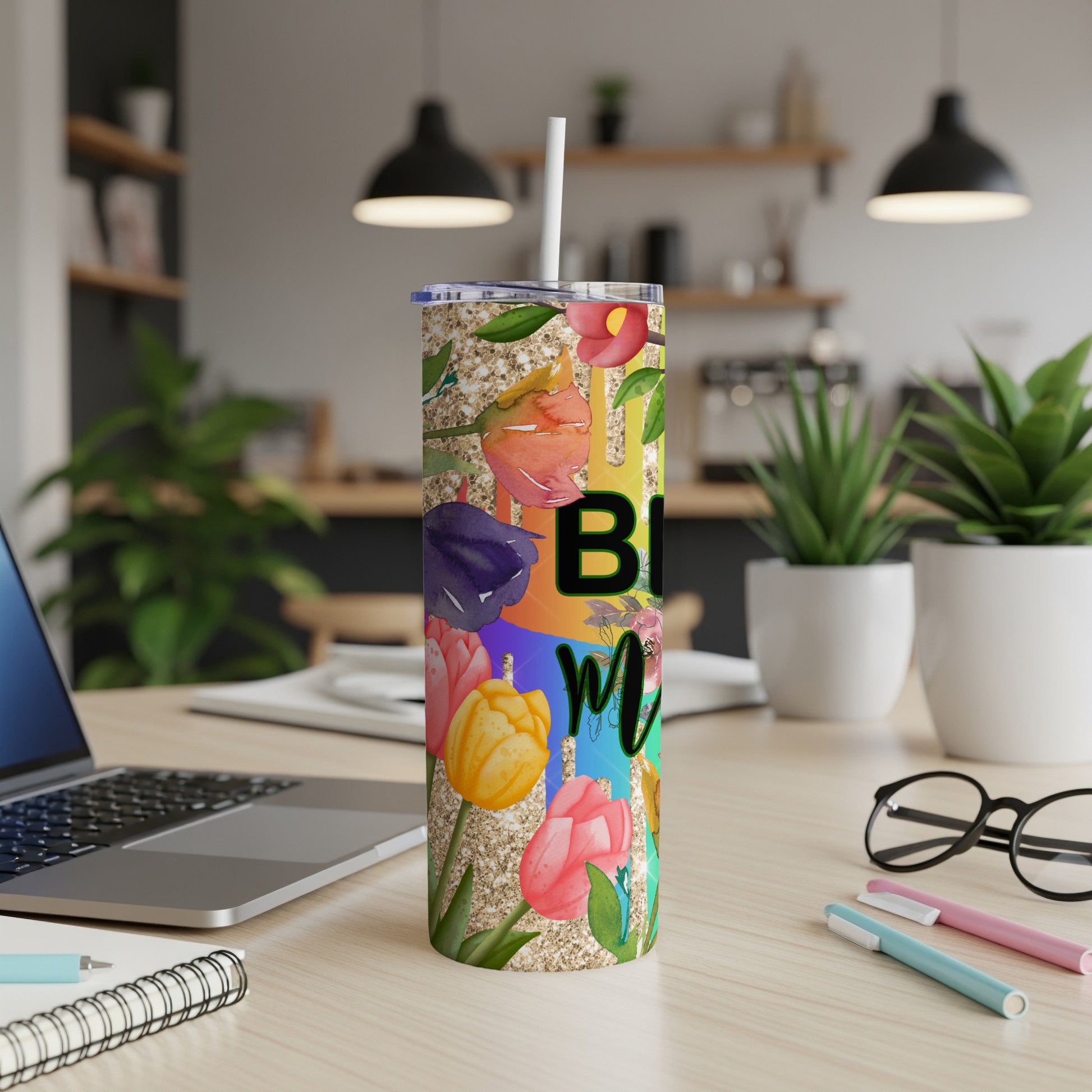 Floral tumbler with "Bloom" text and glitter accents on a desk.