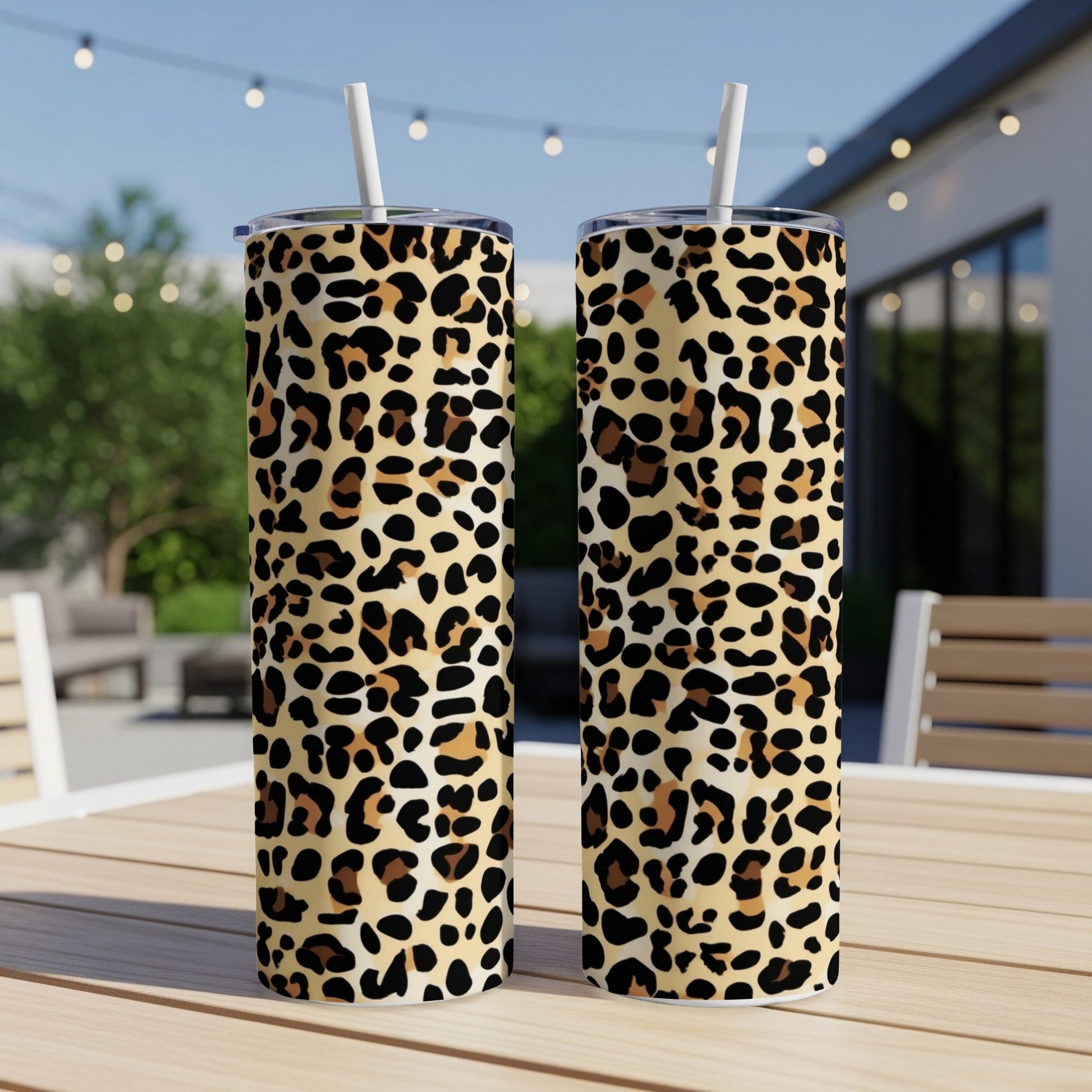 Two leopard print tumblers with straws on a wooden table outdoors.