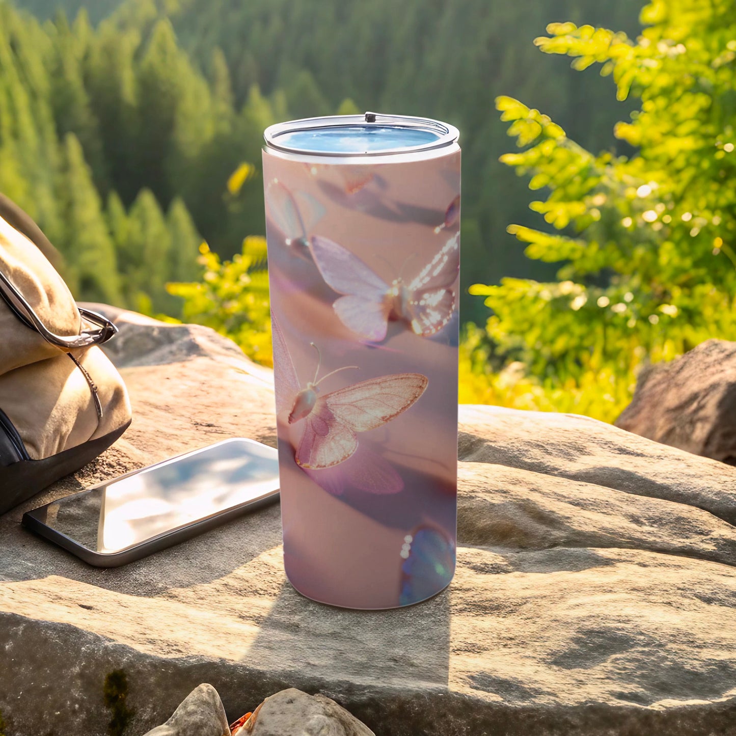 Tumbler with butterfly pattern, resting on rocks with smartphone and backpack.