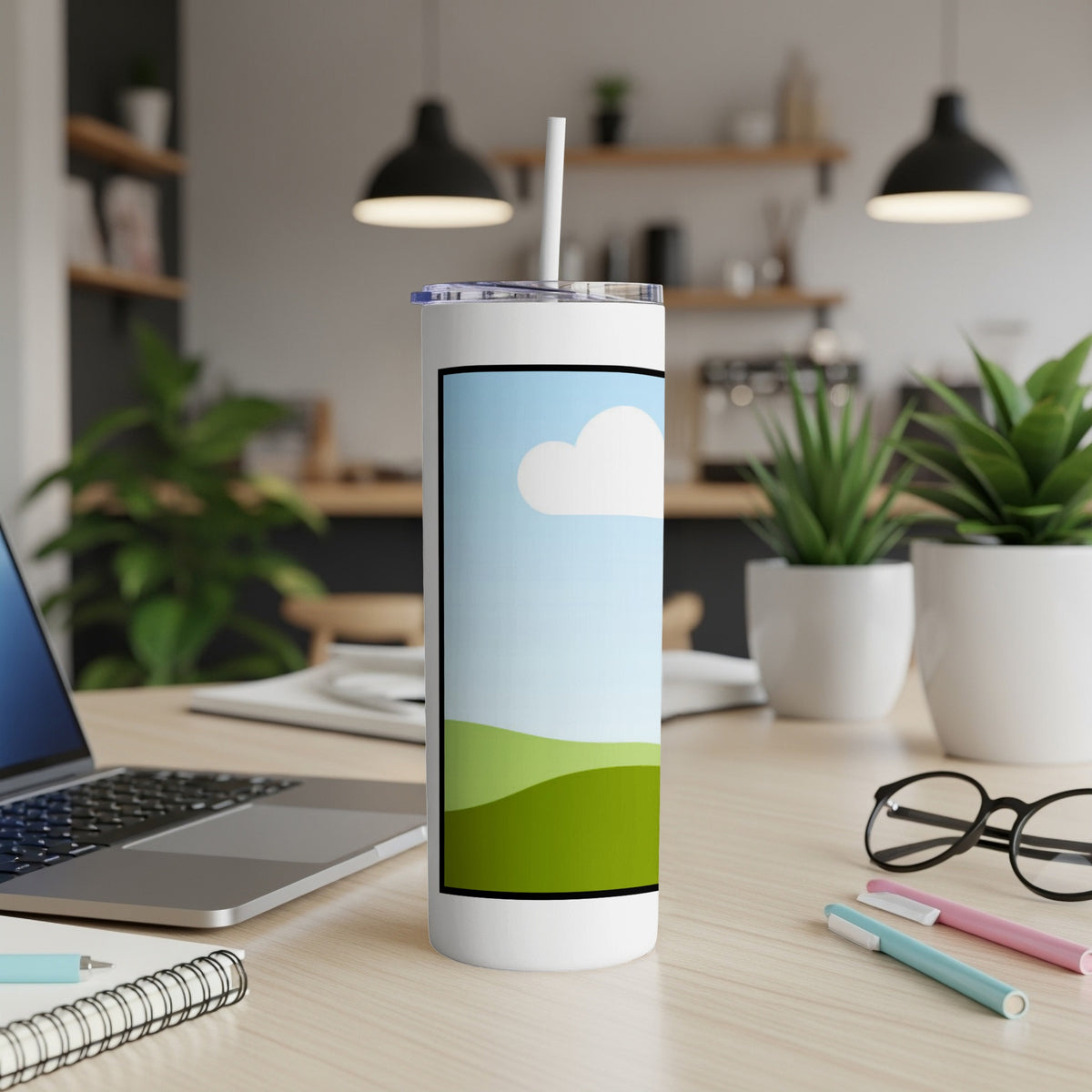 White tumbler with a landscape illustration on a desk with a laptop.