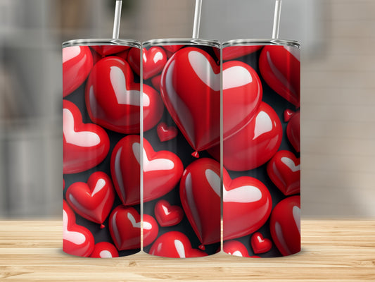 Three red heart-shaped tumblers with straws on a wooden surface.