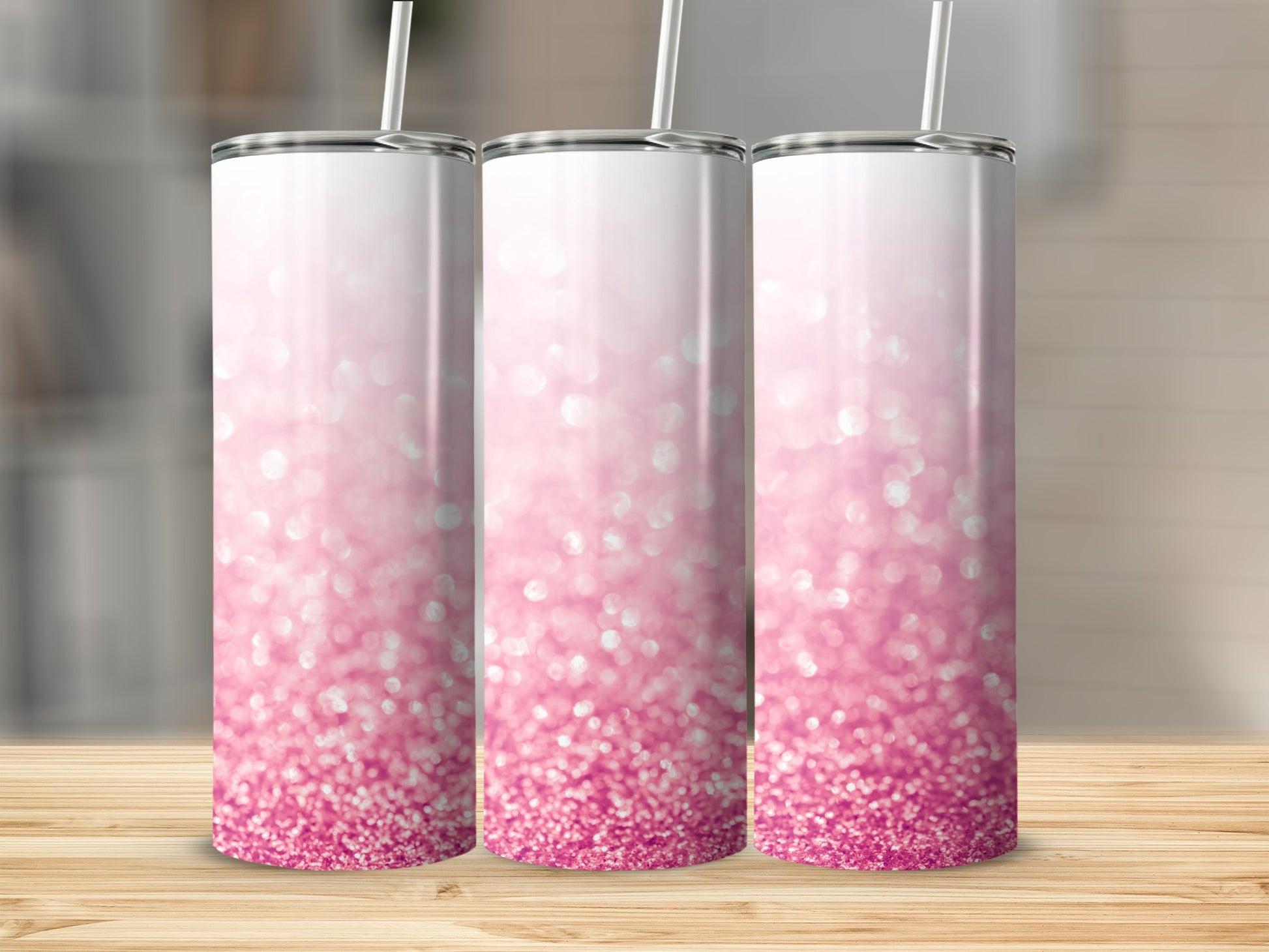 Three pink glitter tumblers with straws on a wooden surface.