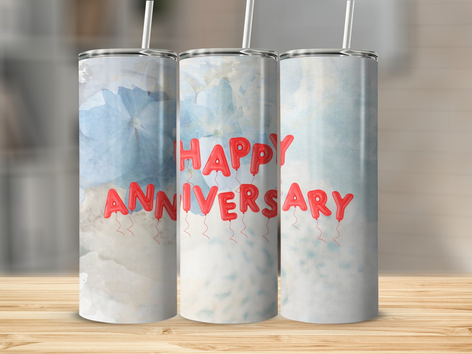 Three tumblers with "Happy Anniversary" text made of balloons on a blurred background.