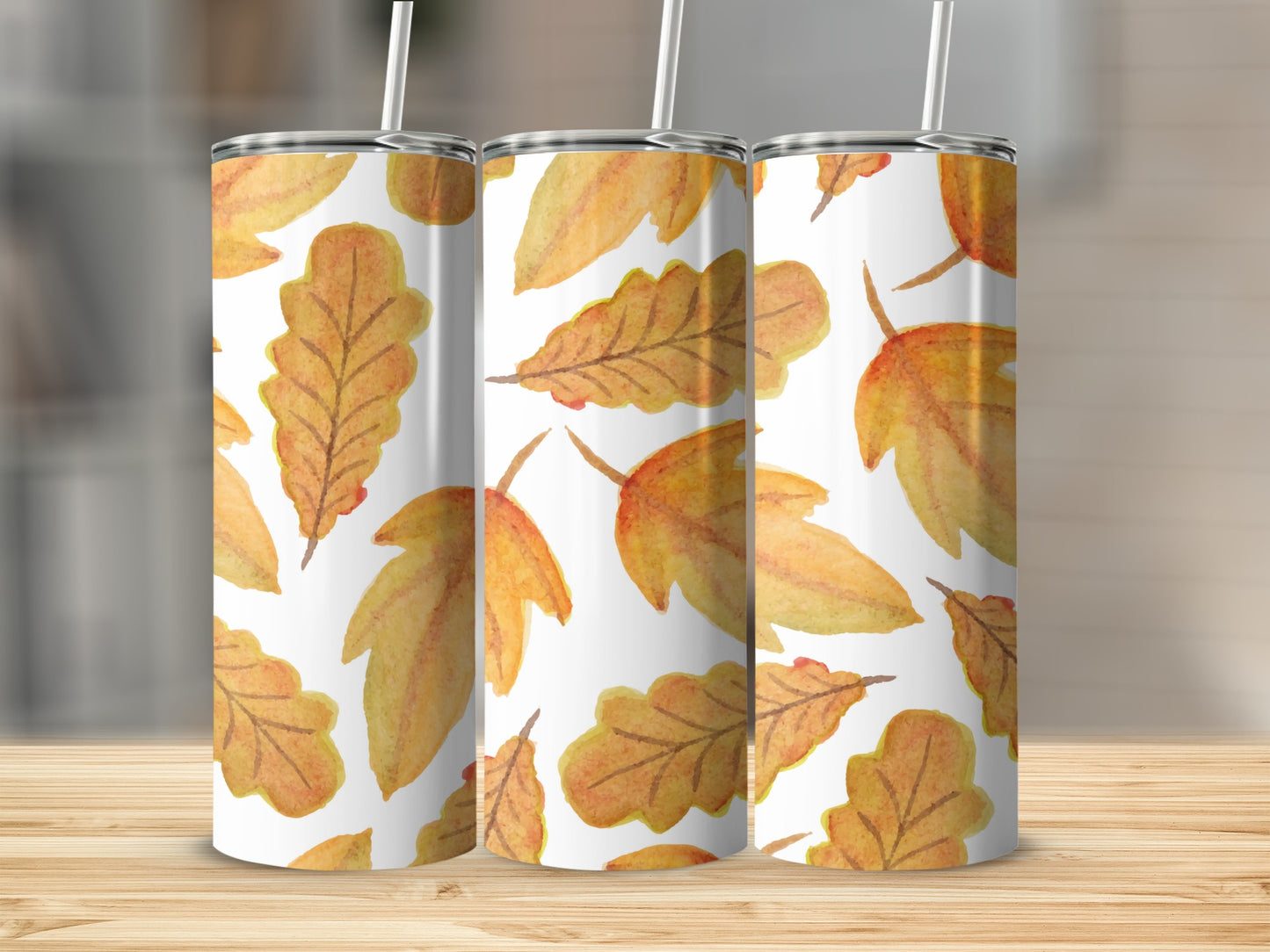 Three tumblers with a repeating pattern of autumn leaves on a wooden surface.