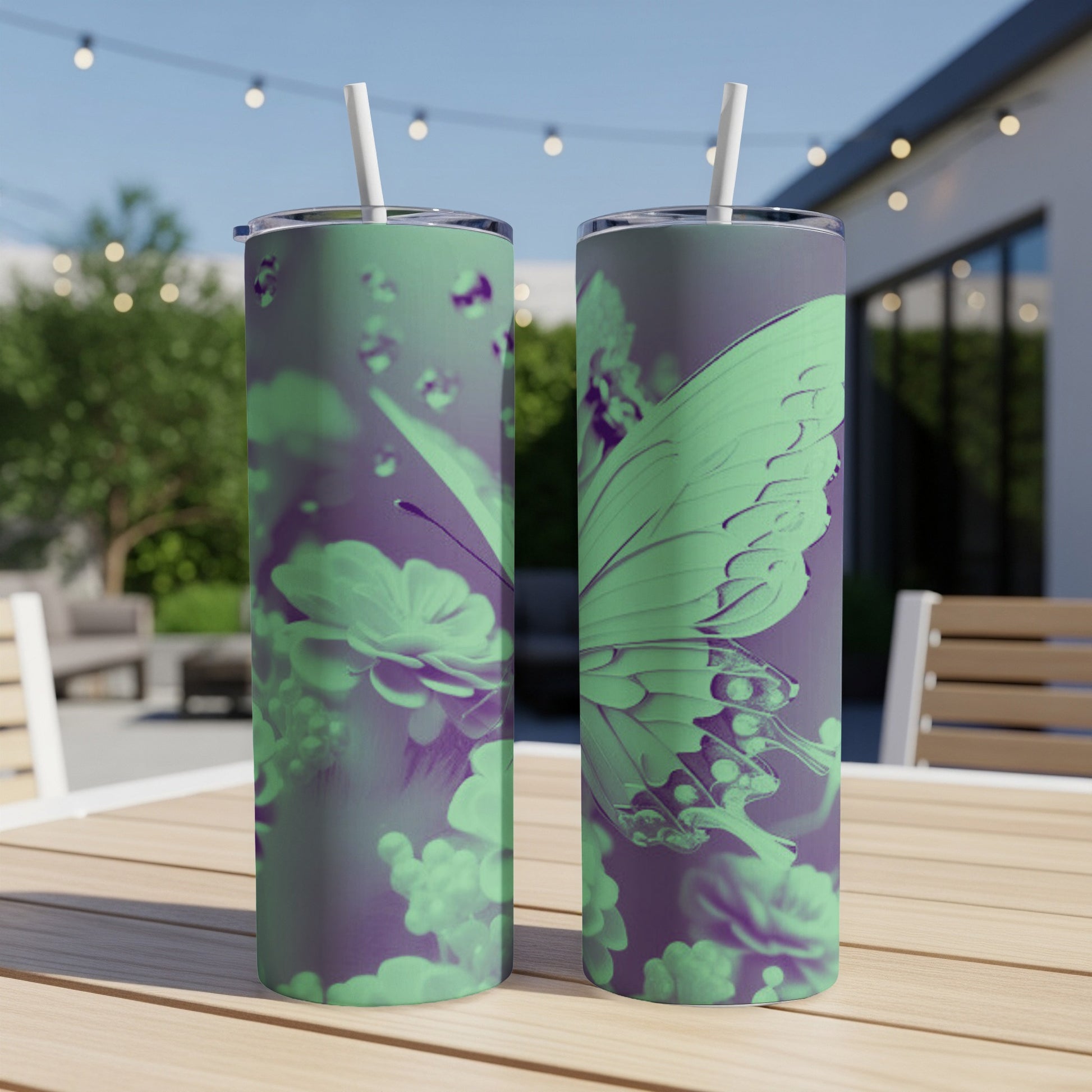 Two mint green tumblers with butterfly and floral design on a patio table.