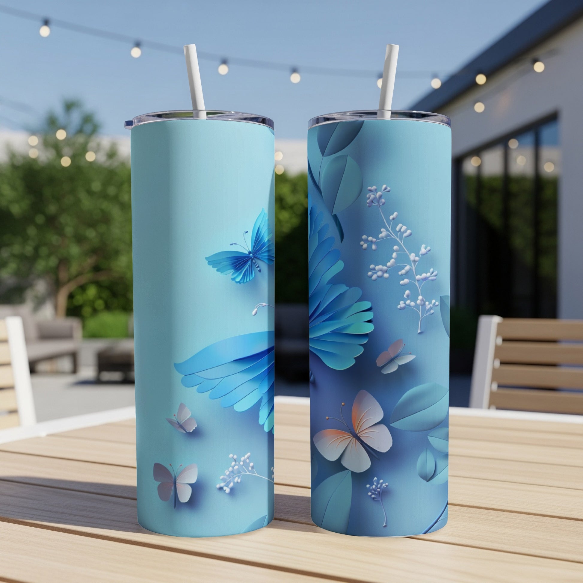 Two blue tumblers with butterfly and floral designs sit on a table outdoors.
