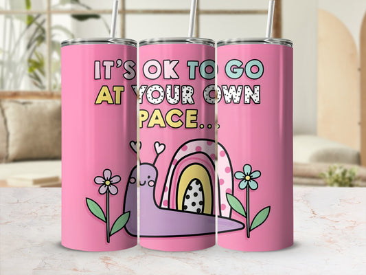 Pink tumbler with a cartoon snail and rainbow, reads "It's ok to go at your own pace..."
