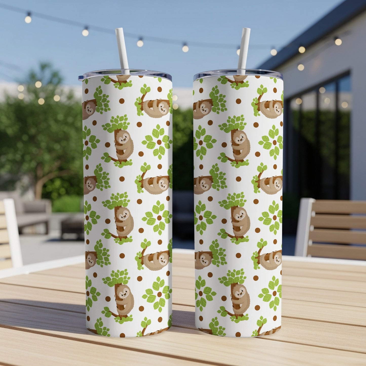Two white tumblers with a scattered sloth and tree pattern sit on a wooden table outdoors.