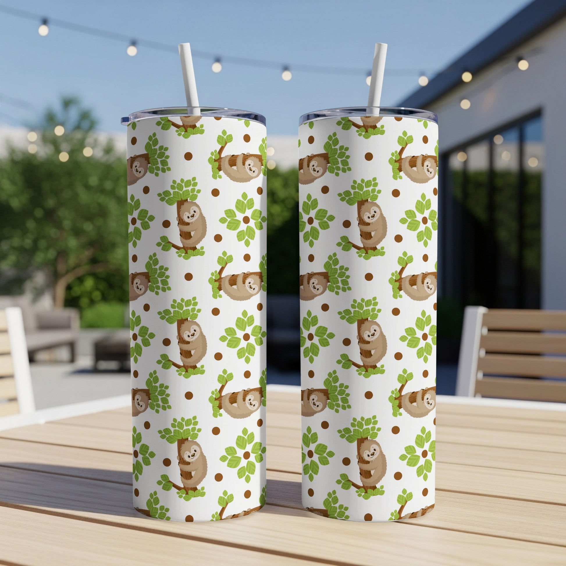 Two white tumblers with a scattered sloth and tree pattern sit on a wooden table outdoors.