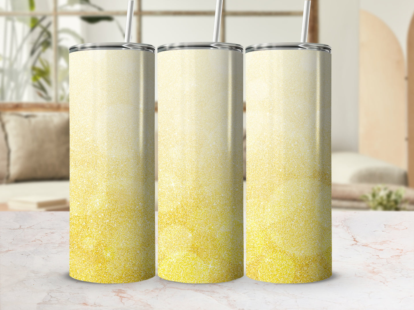 Three glittery gold tumblers with straws on a marble surface.