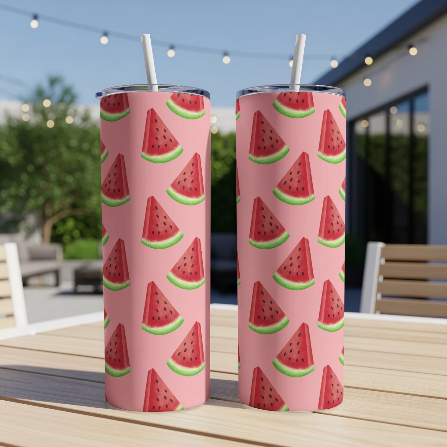 Two pink tumblers with a repeating pattern of watermelon slices on an outdoor table.