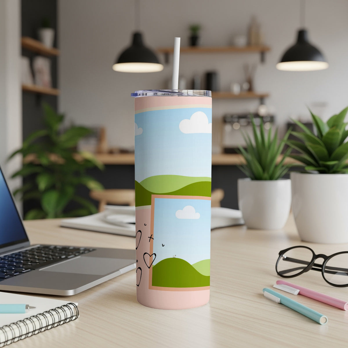 Pink tumbler with landscape and heart design, on a desk.