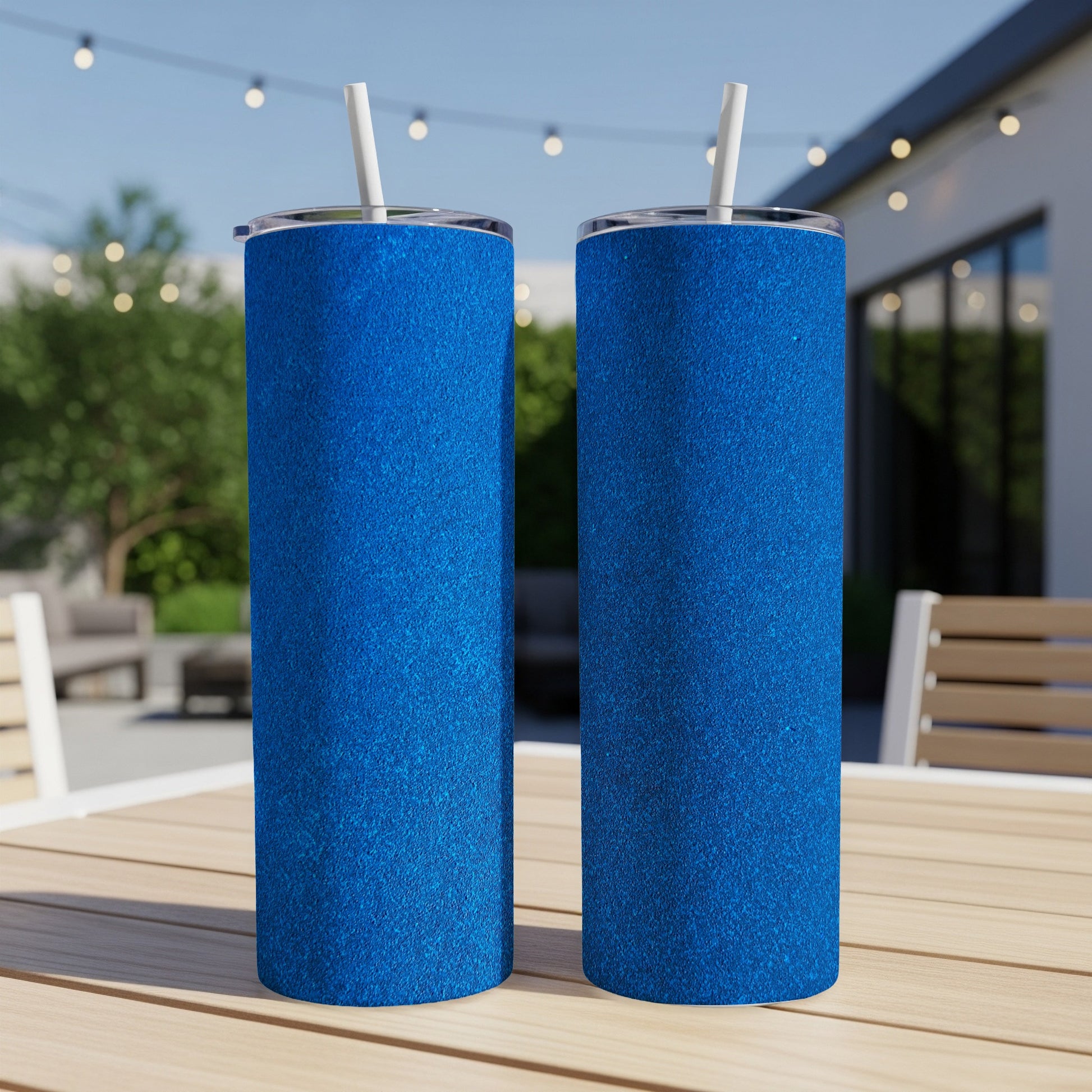 Two blue glitter tumblers with straws on a wooden table.