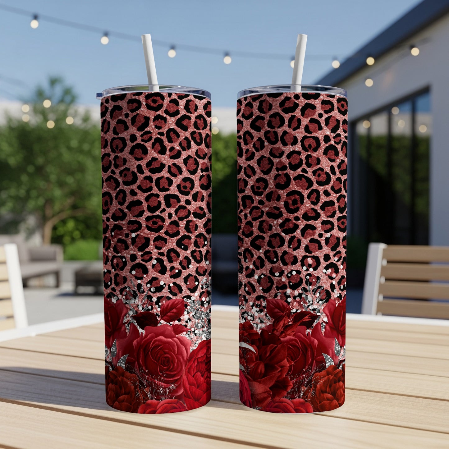 Two red rose and leopard print tumblers with straws on a table.