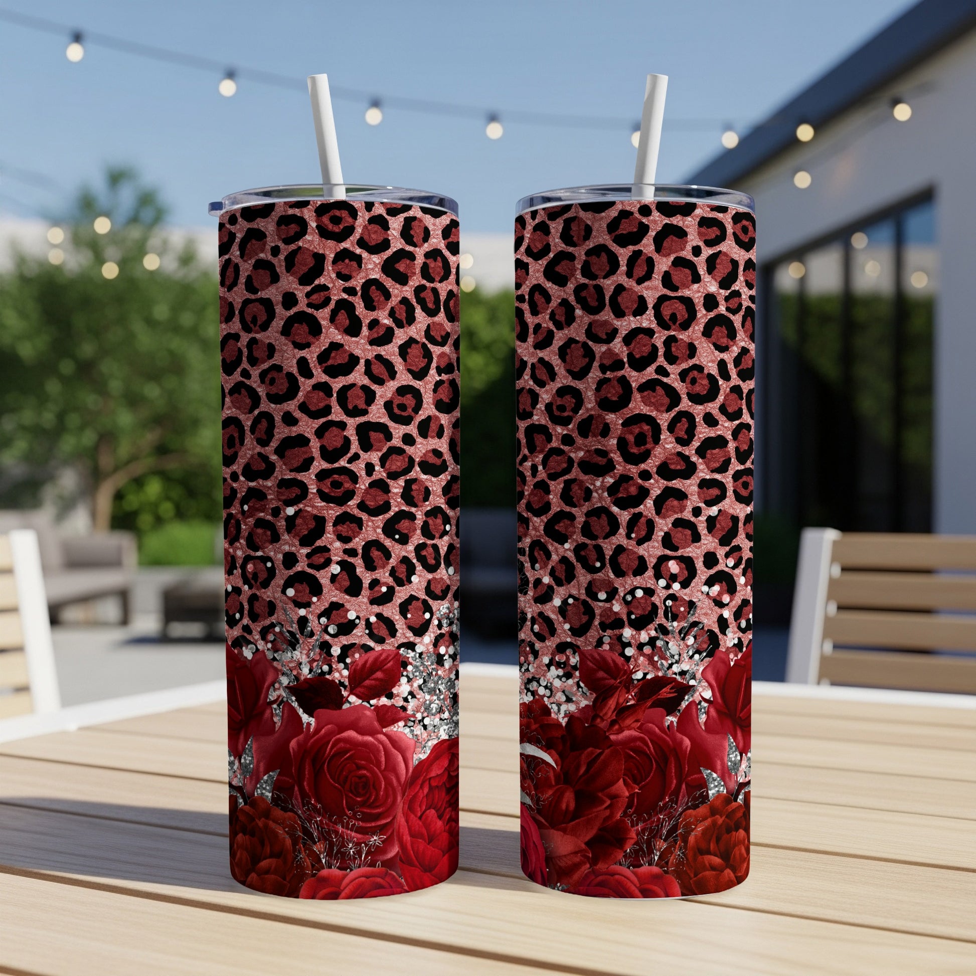 Two red rose and leopard print tumblers with straws on a table.