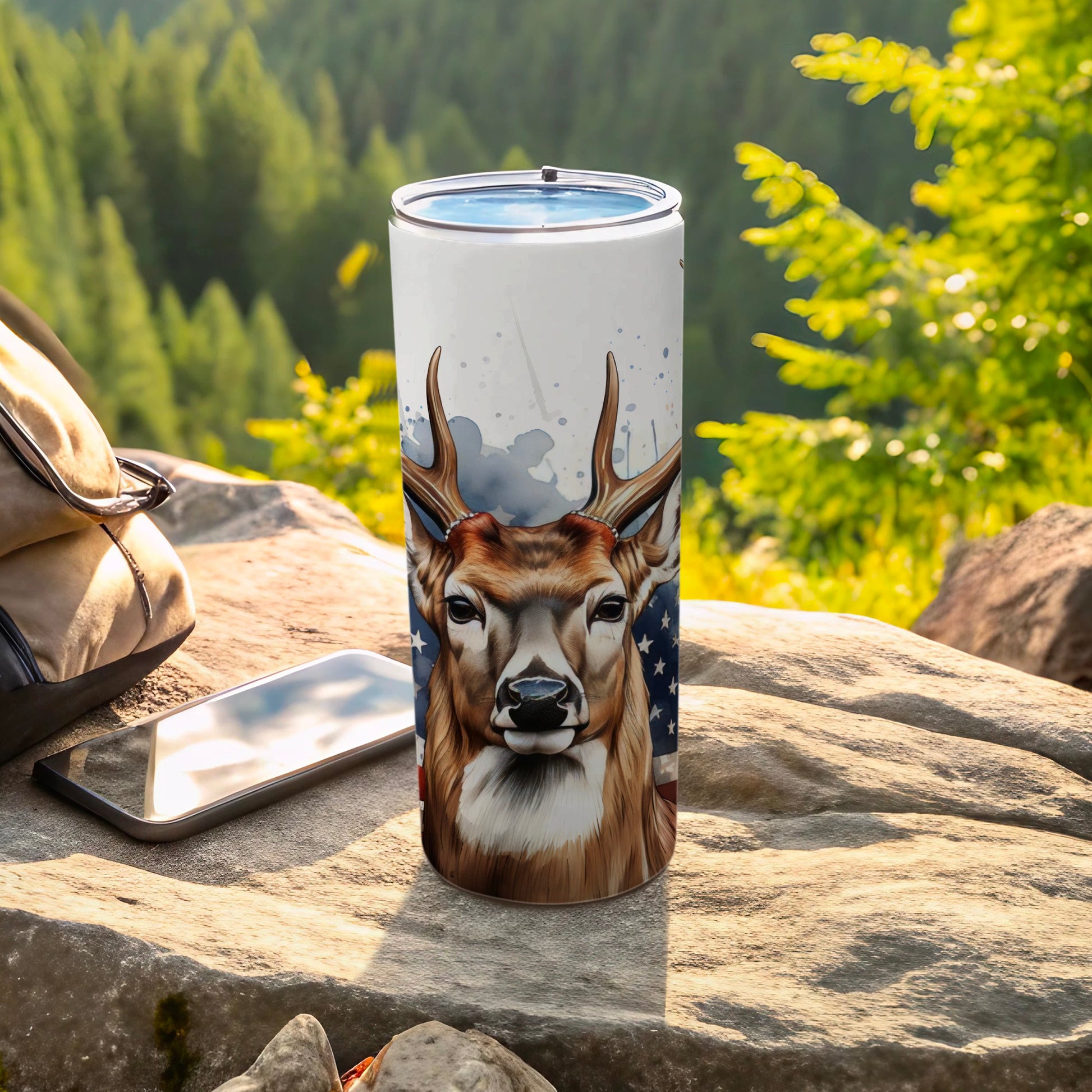Deer head with American flag pattern on a white tumbler with a backpack and phone.