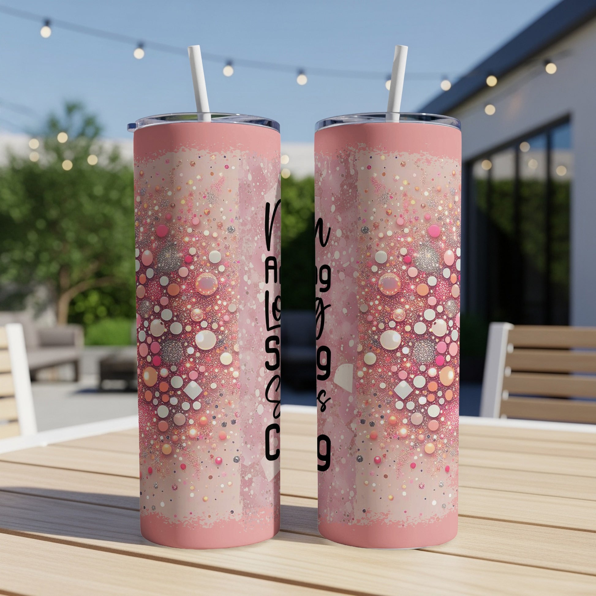 Two pink tumblers with glitter and script text on a patio table.