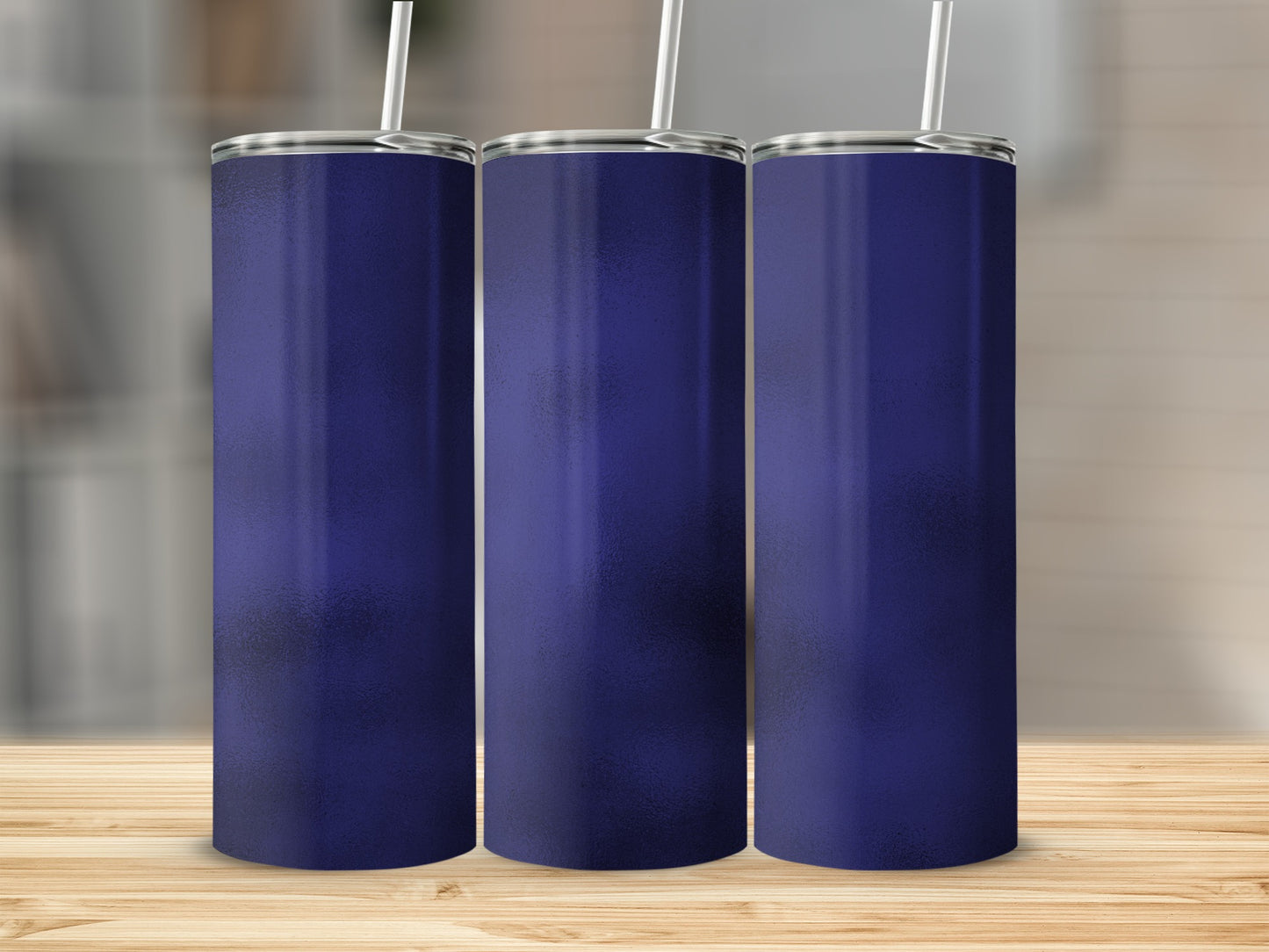 Three navy blue tumblers with straws on a wooden surface.