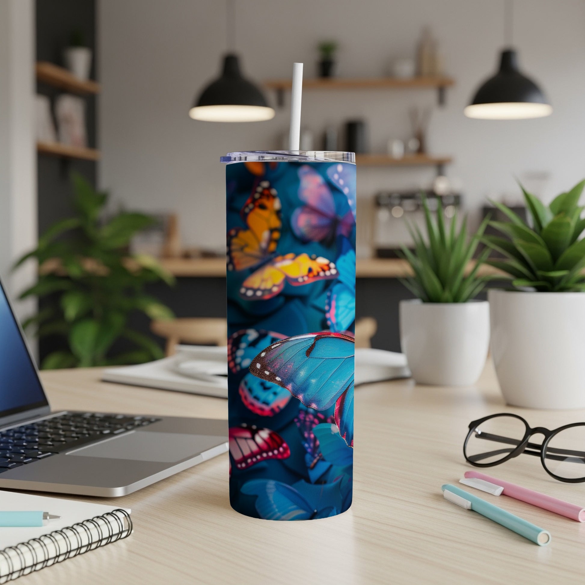 Blue tumbler with colorful butterflies, on a desk with a laptop and pens.